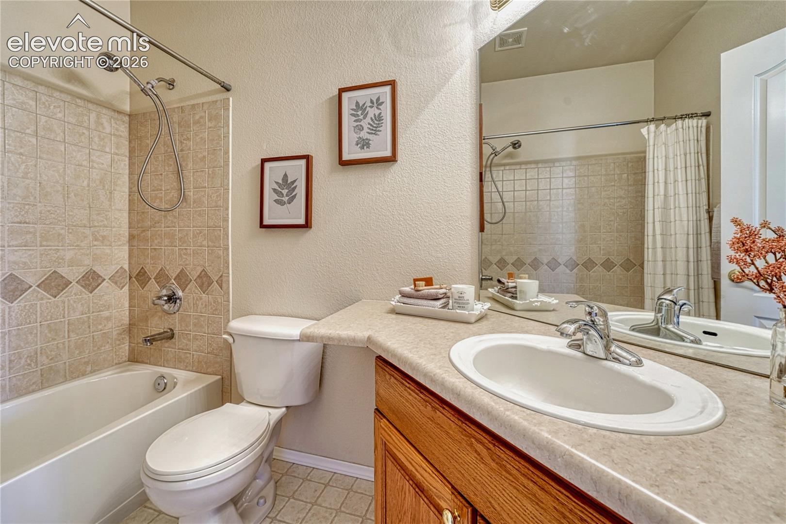 Main-level full bath features an oak vanity, neutral tile-look vinyl flooring, and a tub/shower combination with clean tiled surround
