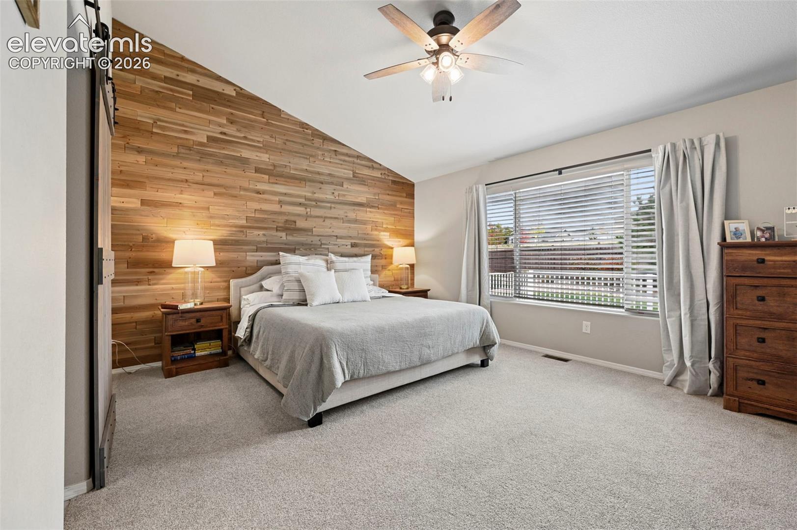 Vaulted ceiling with a wood-plank accent wall, sliding barn door, and a ceiling-mounted light fixture