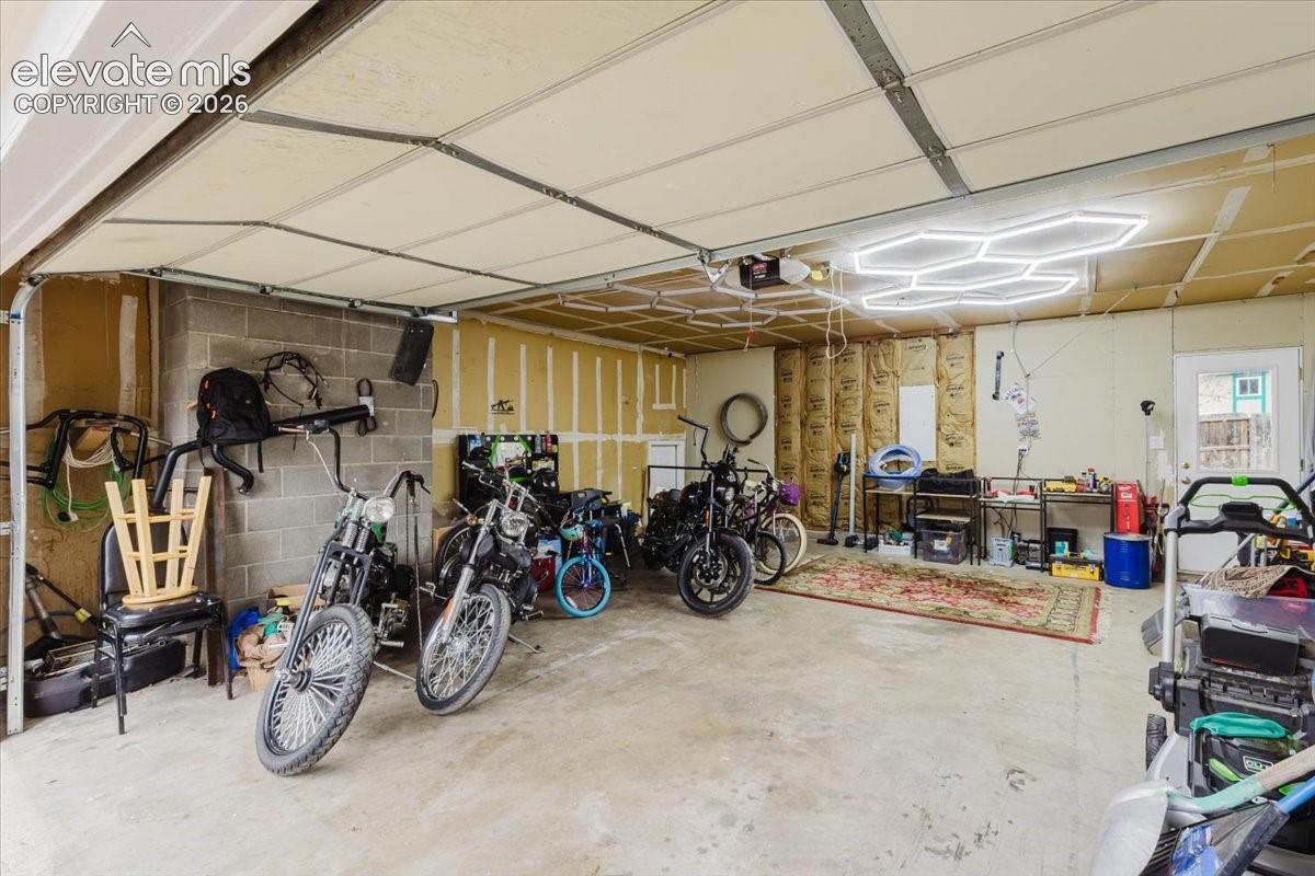 Spacious garage with concrete flooring, exposed insulation, a privacy door, and modern hexagonal ceiling lighting