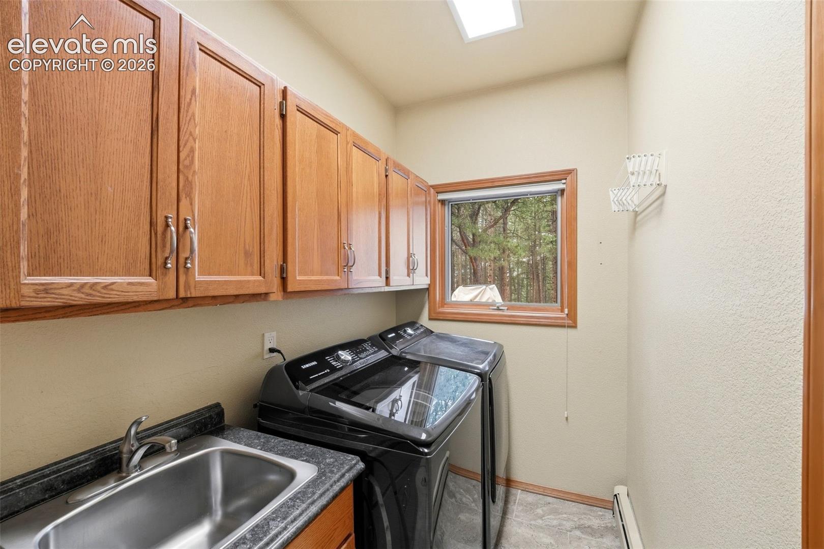 Utility room featuring wood-finish cabinetry with silver-tone hardware, a stainless steel sink with a single-handle faucet, dark stone-finish countertops, and durable flooring