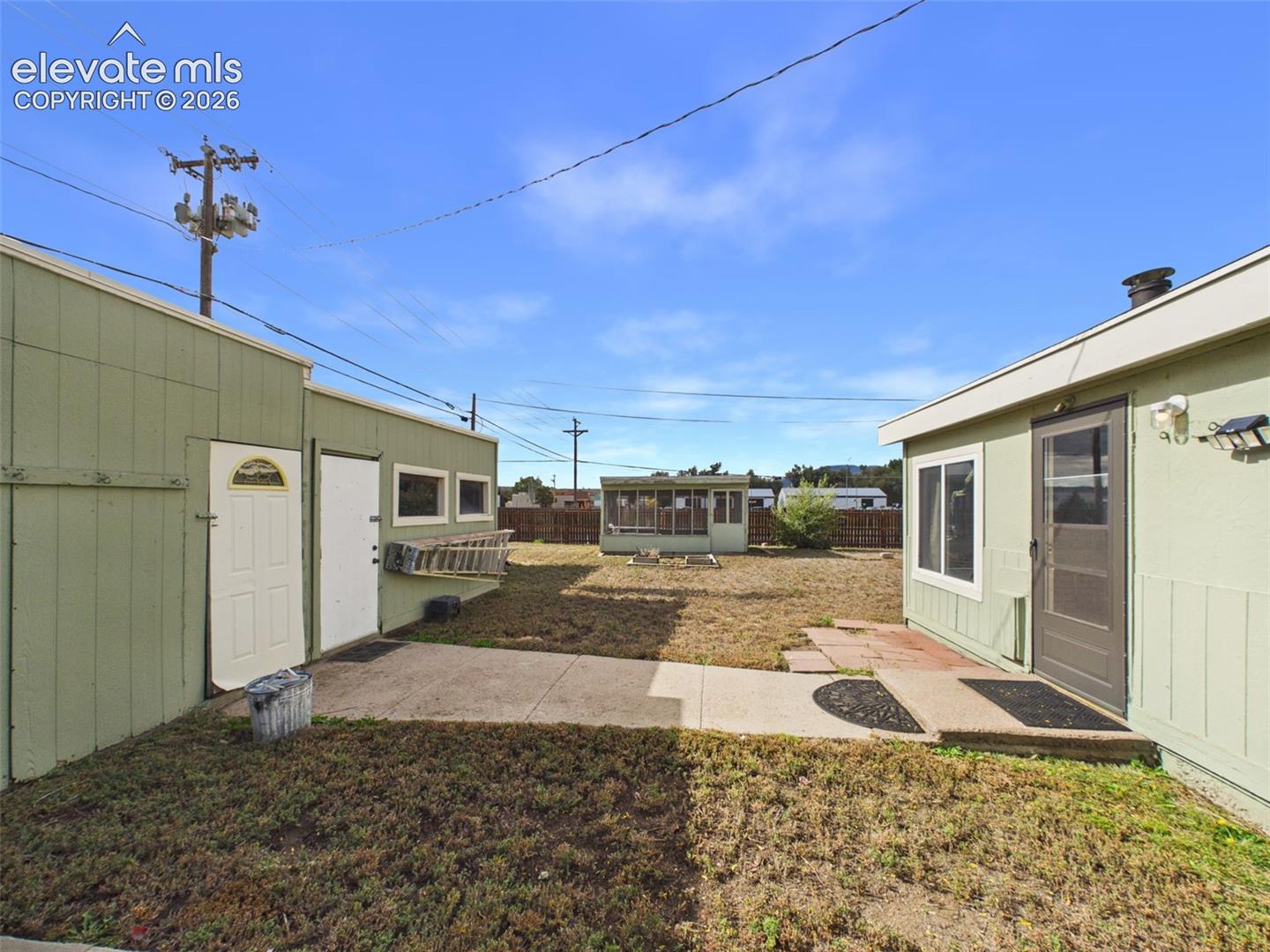 Spacious backyard featuring concrete walkways, multiple detached outbuildings, and an enclosed outdoor structure, offering plenty of possibilities for storage, hobbies, and outdoor activities.