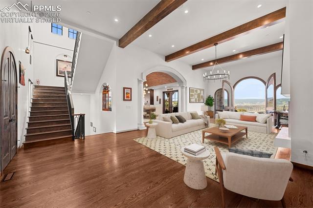 Beautiful great room with soaring ceilings, exposed beams, and arched doors opening to mountain view, with a layout flowing into the kitchen and dining areas. Virtually staged.