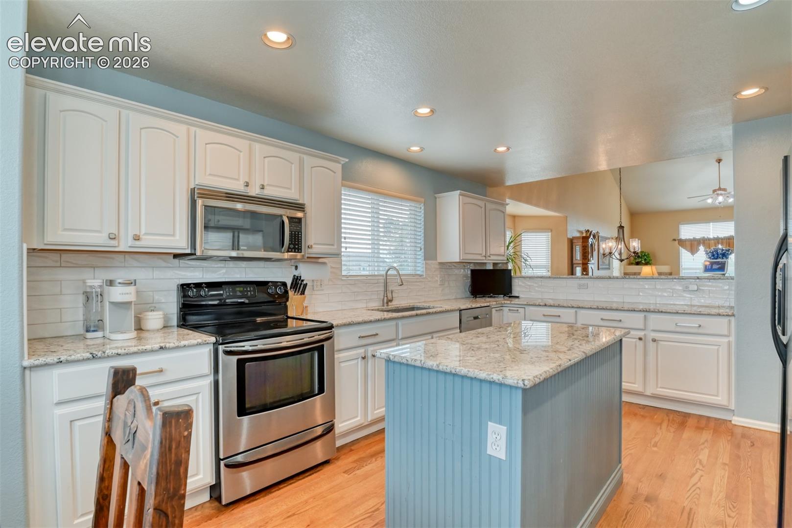 White cabinetry with chrome hardware, subway tile backsplash, stainless steel appliances, speckled countertops, and a center island with beadboard detailing