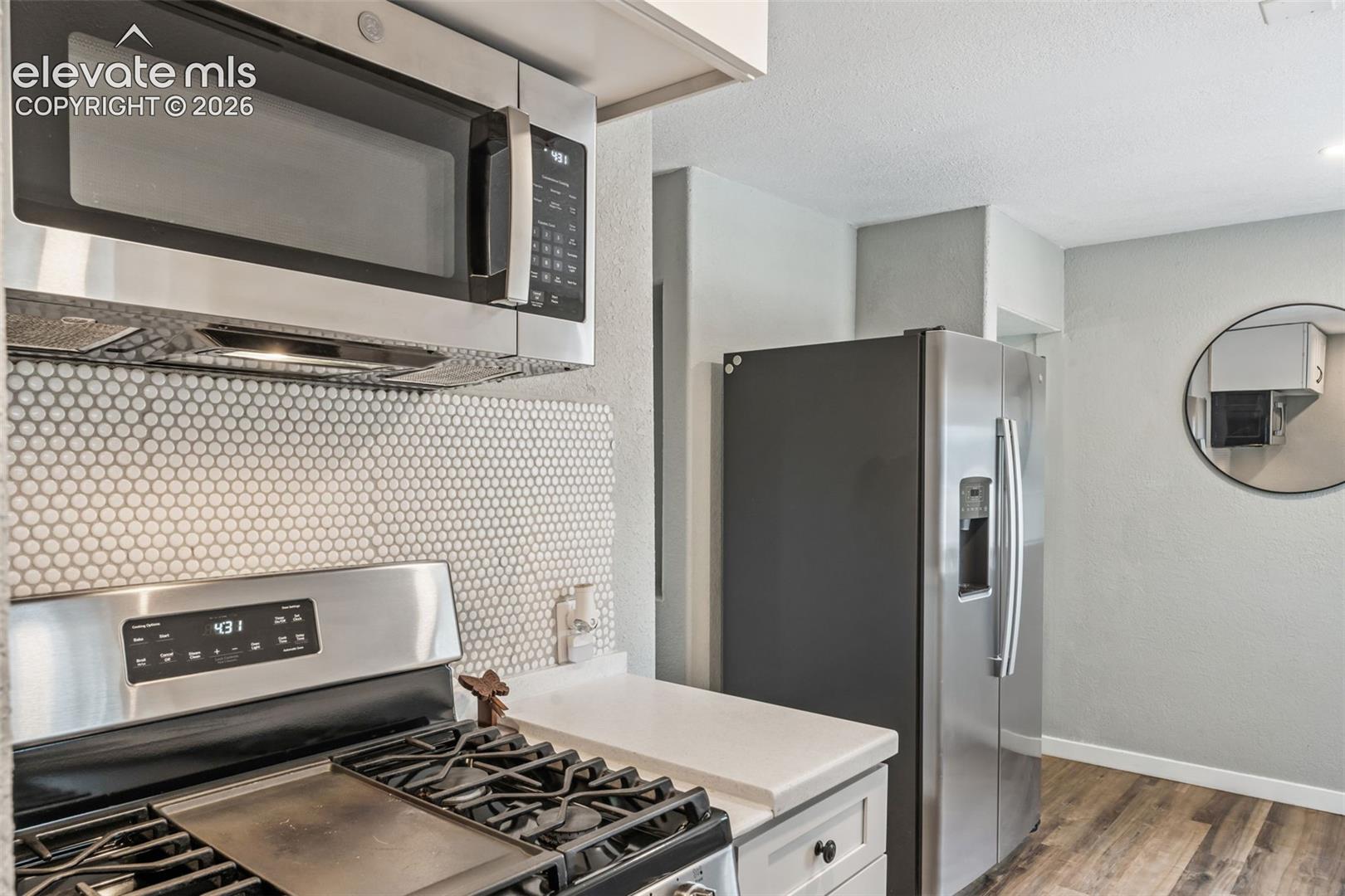 Kitchen featuring stainless steel appliances, white penny tile backsplash, white countertops, light wood-finish flooring, and light gray walls