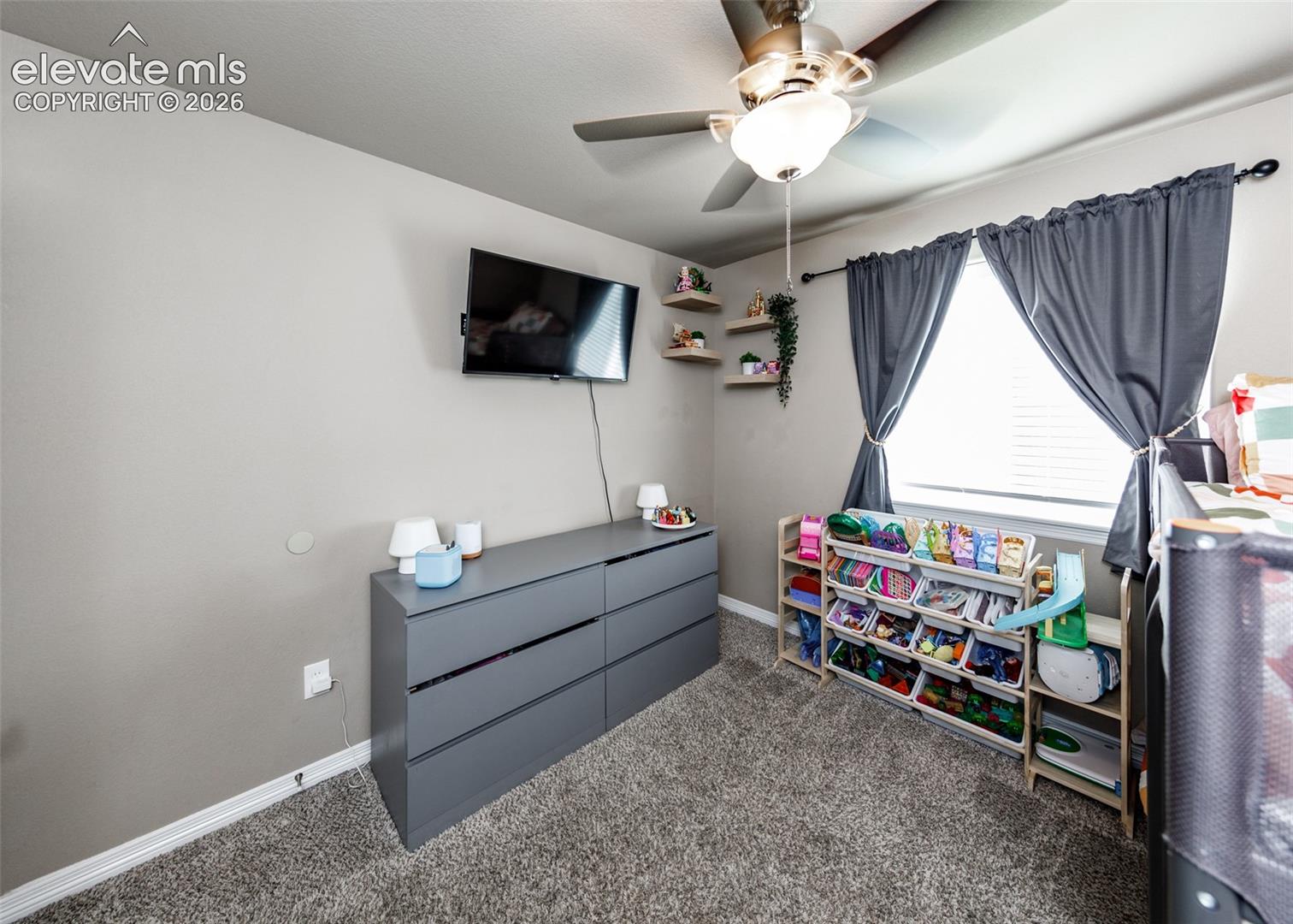 Carpeted flooring, brushed nickel ceiling fan with integrated light fixture, and two wall-mounted floating wood shelves
