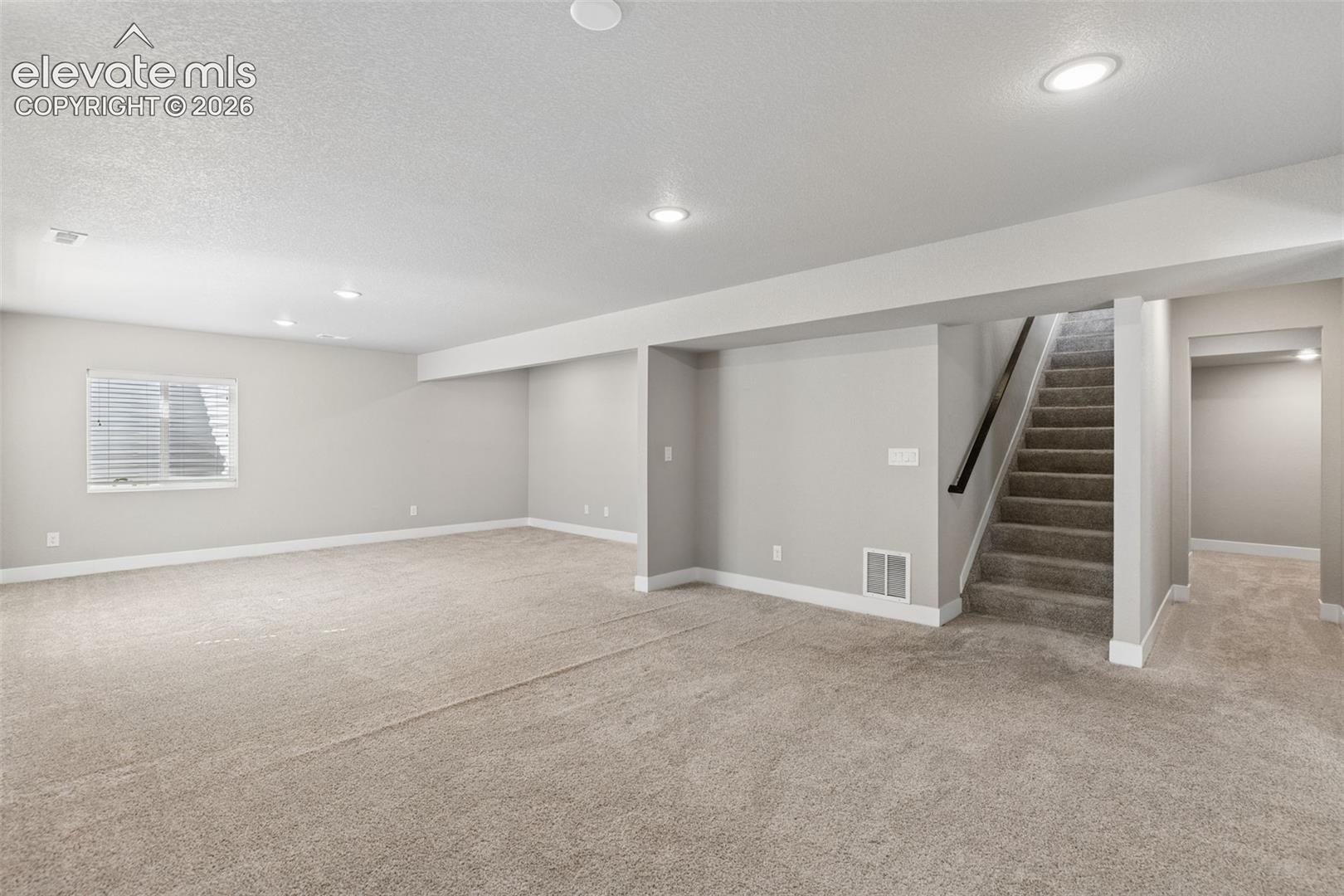Open floor plan featuring neutral wall tones, wall-to-wall carpeting, recessed lighting, and a staircase with a dark wood handrail