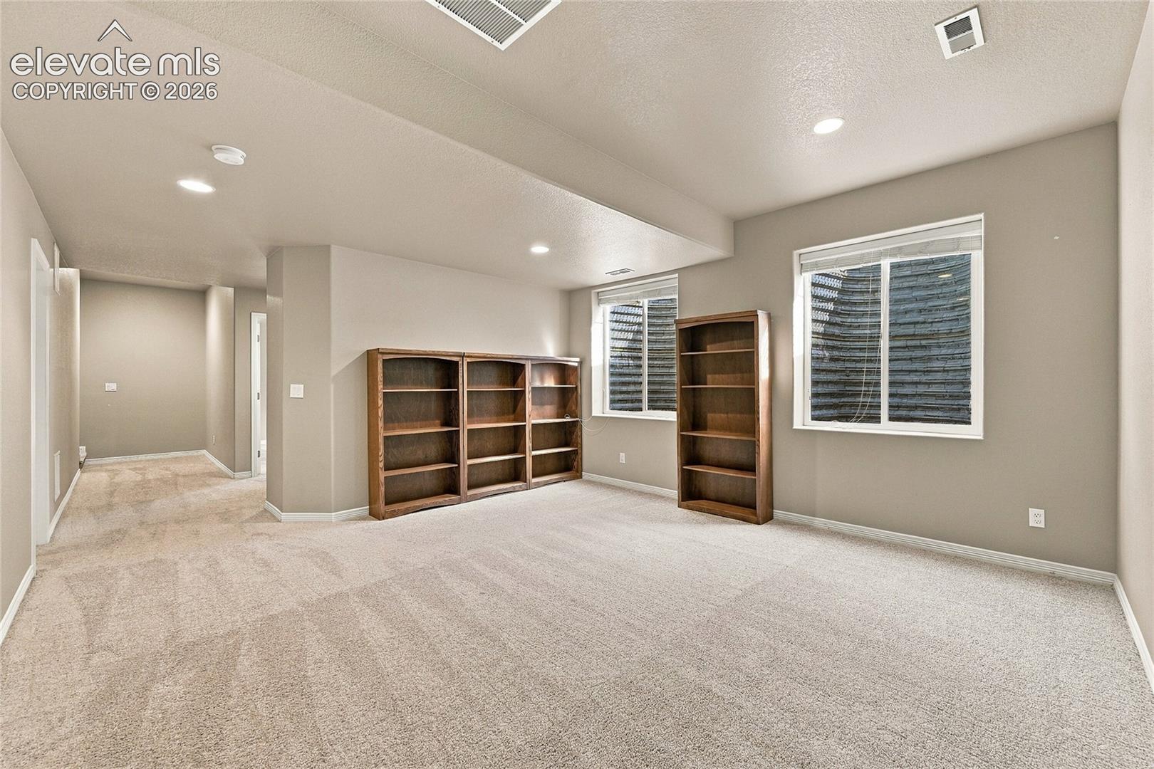 Neutral-toned interior space featuring built-in wooden shelving units, recessed ceiling lighting, wall-to-wall carpeting, and double-pane windows