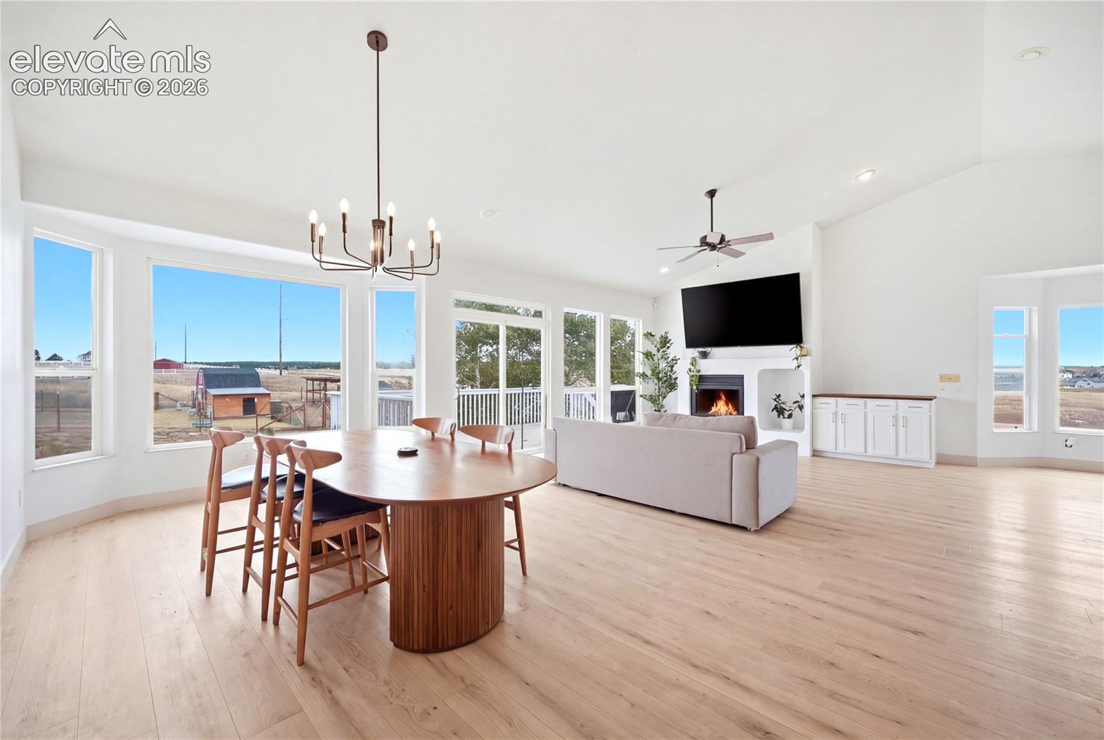 Open-concept interior featuring vaulted ceilings, wood-finish flooring, a floor-to-ceiling fireplace with integrated shelving, and large picture windows