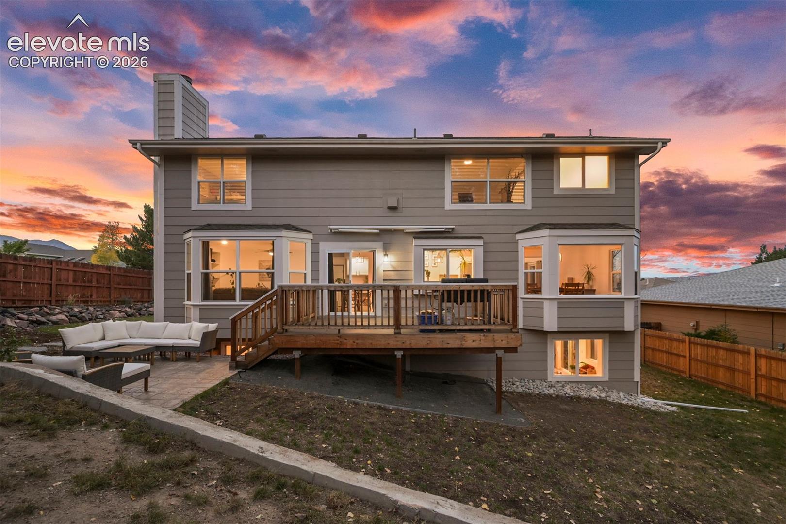 Multi-level rear exterior featuring a wood deck, lower patio, and bay windows