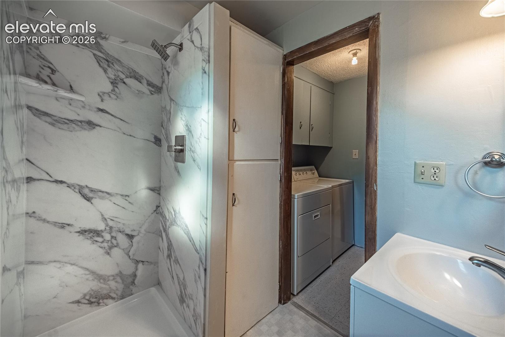 Shower enclosure featuring large-format stone-patterned wall tile and a built-in recessed shelf