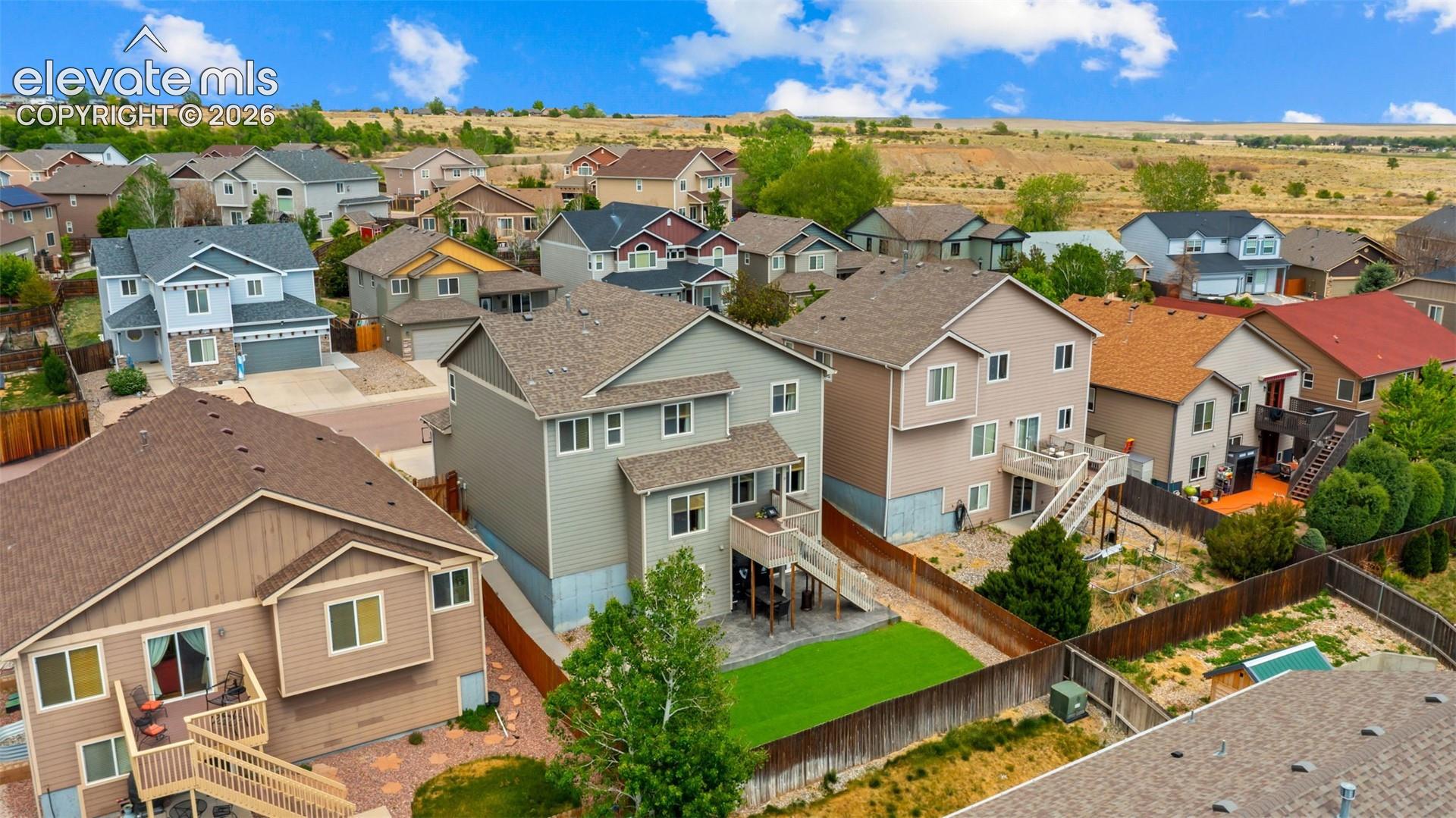 Rear exterior featuring a two-story design, attached deck with stairs, fenced yard with artificial turf, and stamped concrete patio area