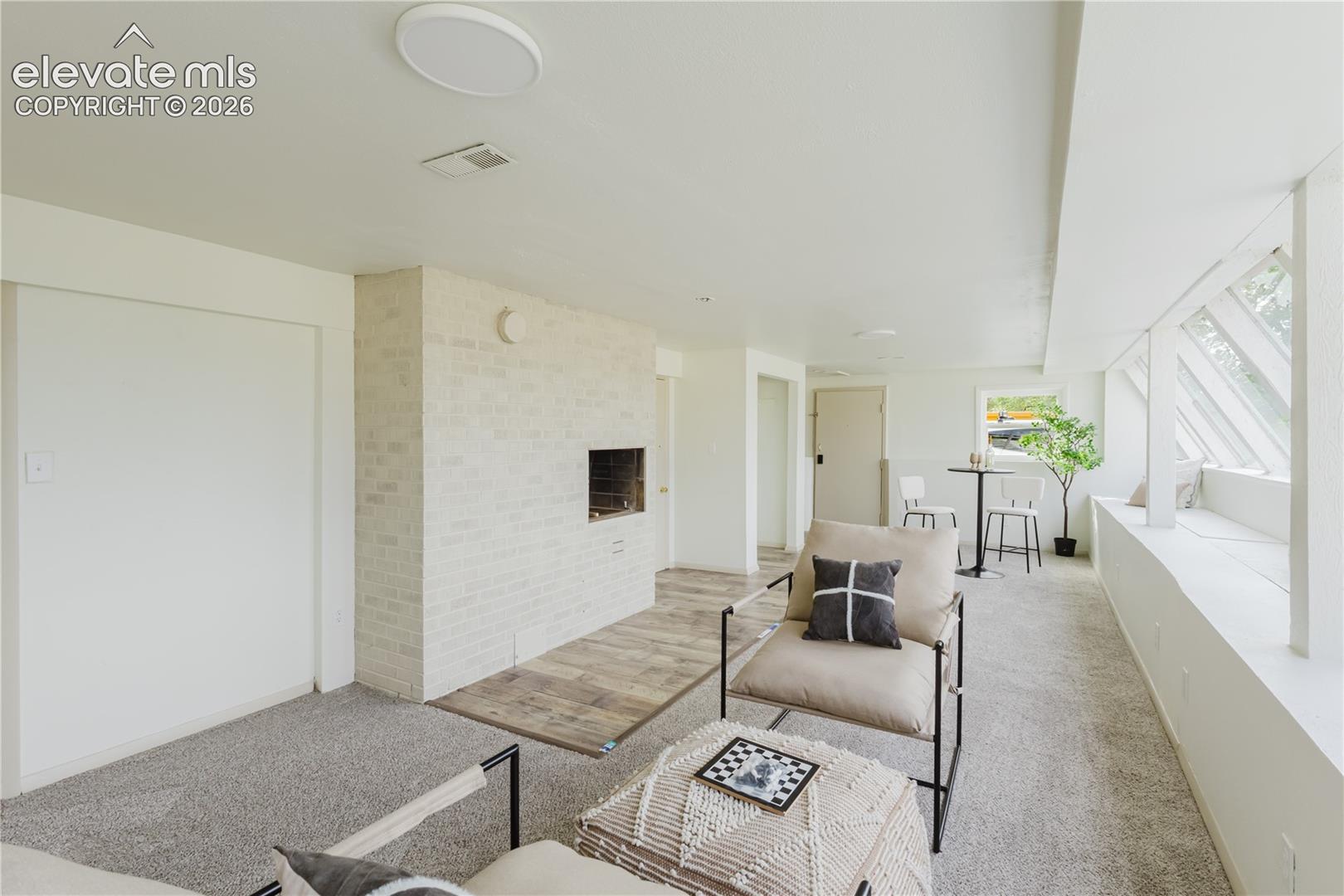 Living area featuring a white-painted brick fireplace with a wood-finish hearth, gray carpet, and a built-in window bench