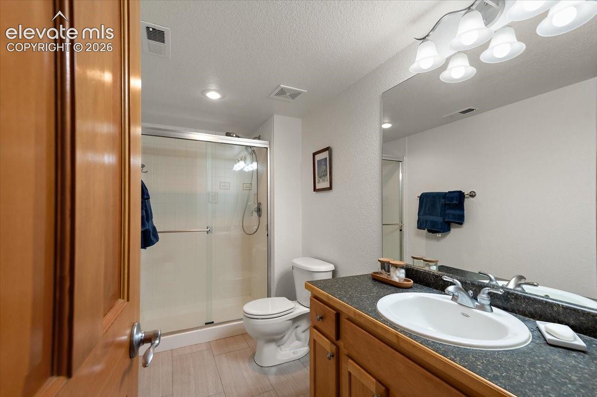 Basement bathroom featuring a wood-finish vanity with an integrated sink, a dark countertop, a large mirror, and overhead lighting