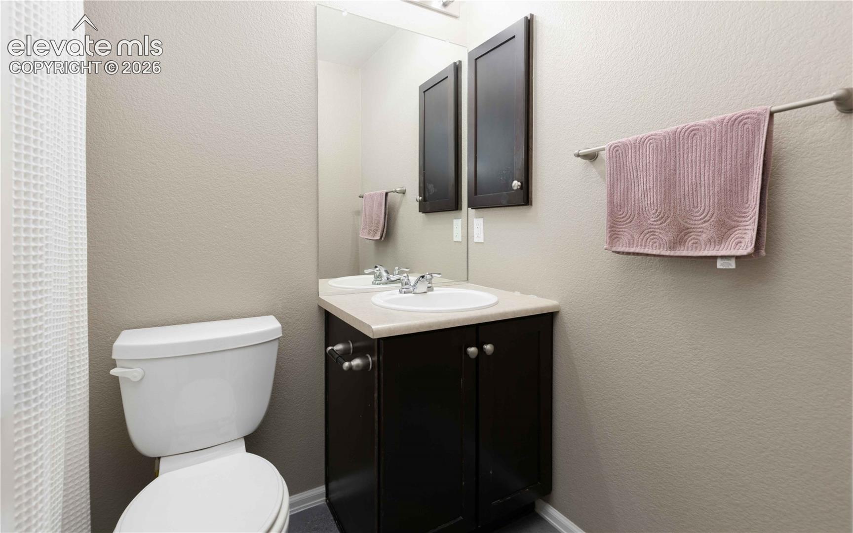 Vanity with dark-finish cabinetry, solid-surface countertop, integrated oval basin, and wall-mounted mirror