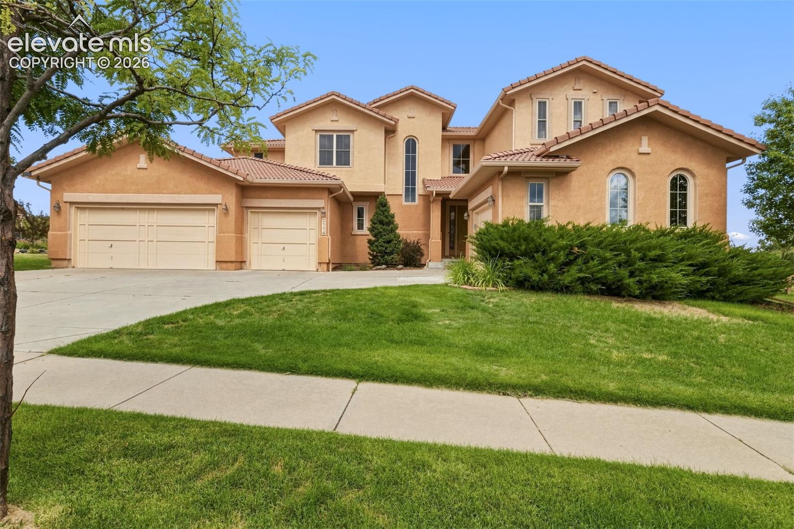 Stucco exterior featuring multiple arched windows, a multi-car garage, and a tile roof