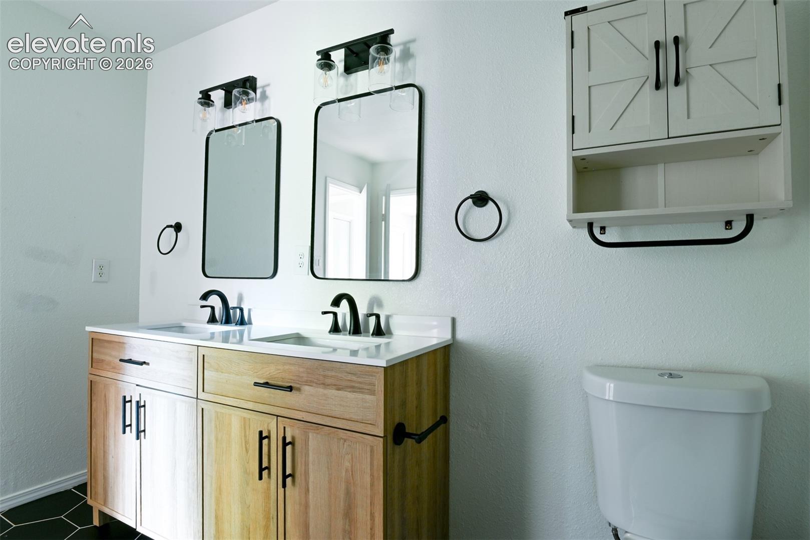 Dual vanity with wood-finish cabinetry, white countertop, and matte black fixtures