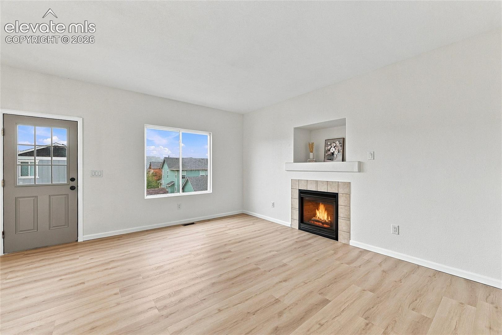 Interior space featuring wood-finish flooring, a tile-surround fireplace, a built-in recessed niche, a sliding window, and a door with a multi-pane glass insert