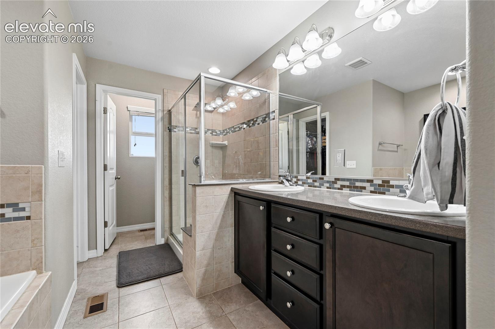 The en-suite 5-piece master bathroom is wrapped in decorate ceramic tile with a high-counter dual vanity and ample lighting.