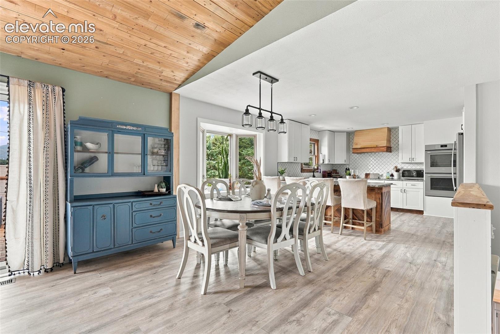 Vaulted wood-paneled ceiling, light wood-finish flooring, recessed lighting, double wall ovens, and a kitchen island with seating