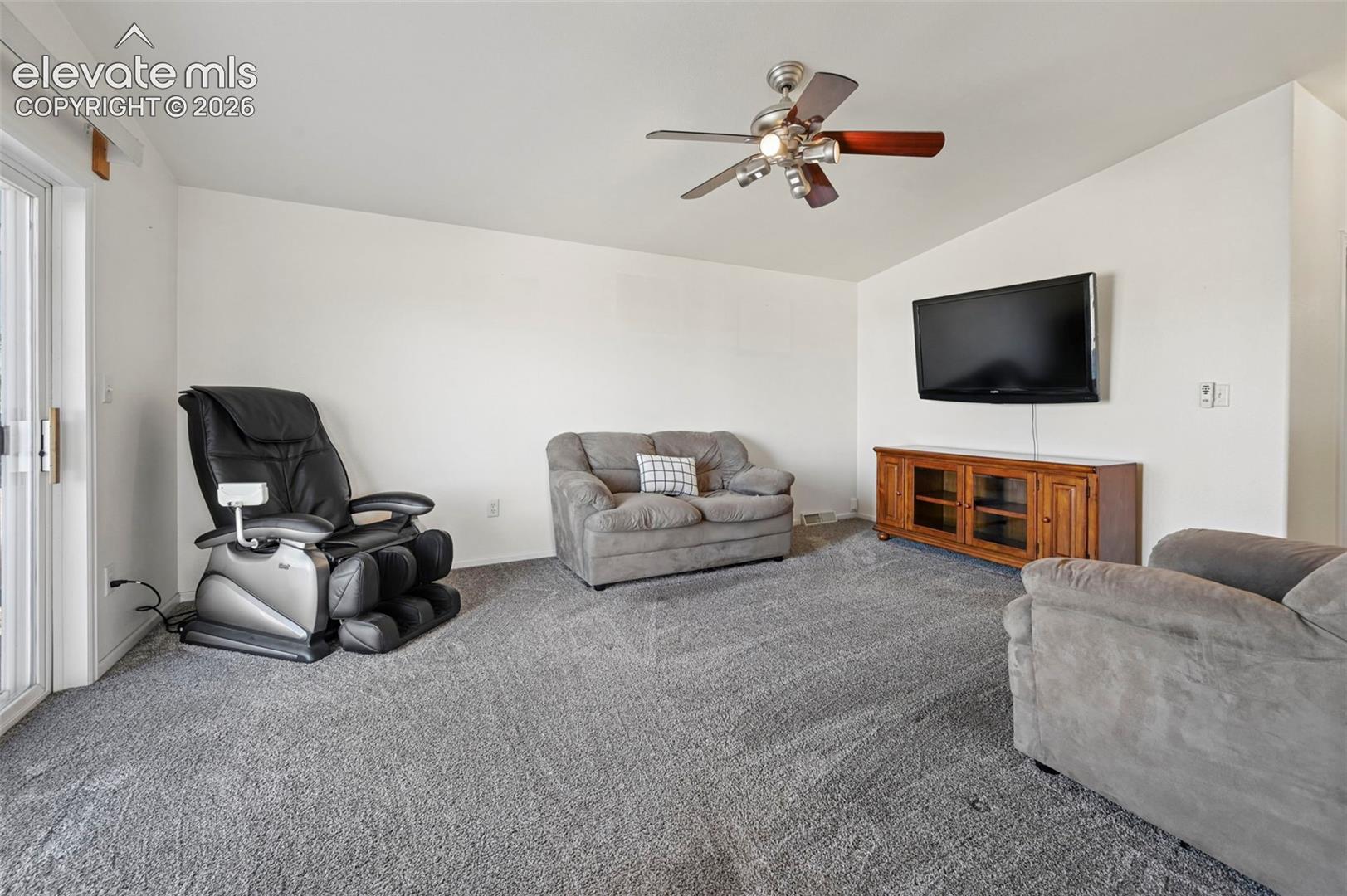 Sliding glass door, wall-mounted television, wooden media console, and ceiling fan with integrated lighting