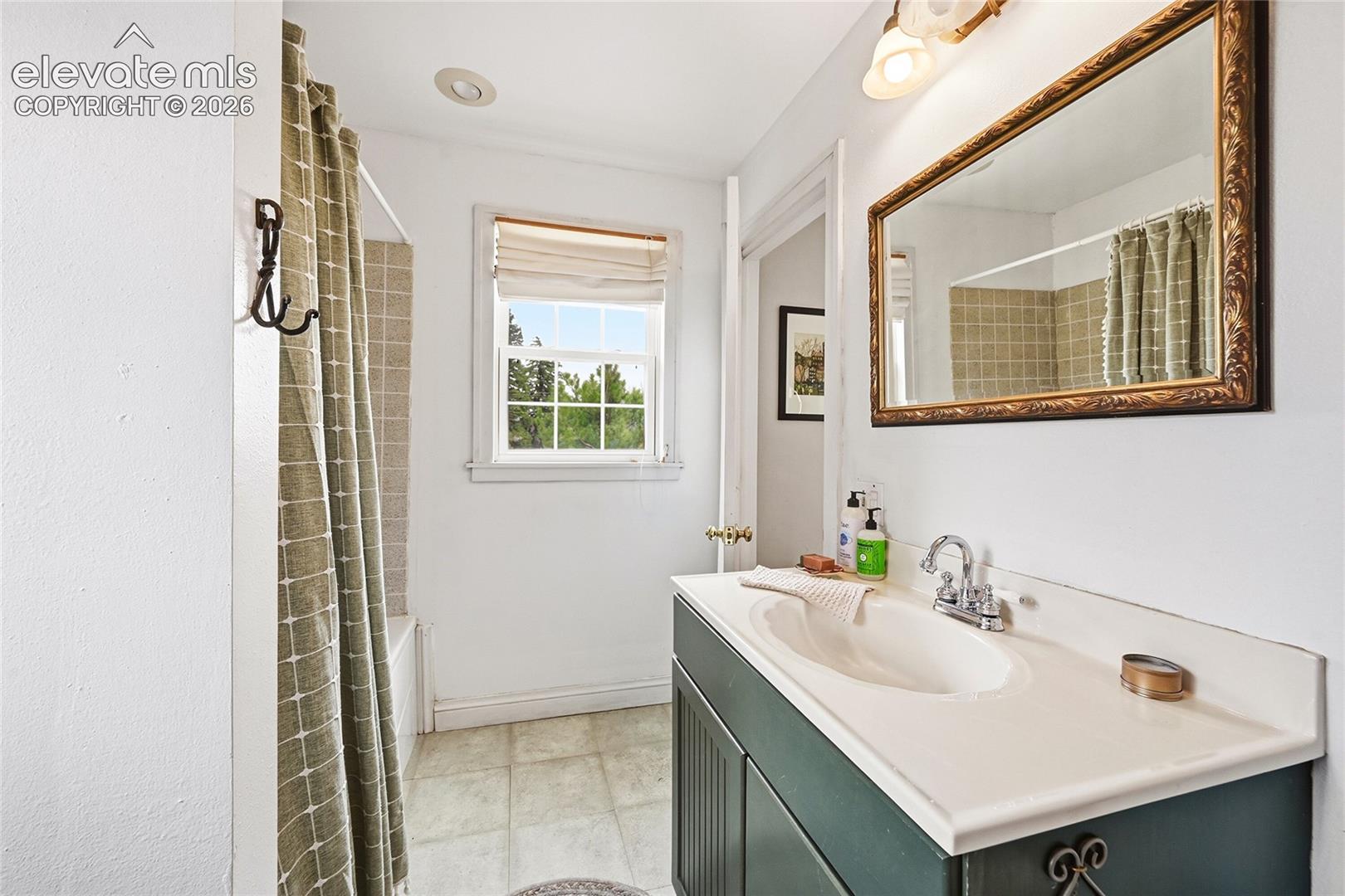 Bathroom featuring a vanity with an integrated sink, brushed-nickel faucet, framed wall mirror, tiled tub surround, and multi-pane window