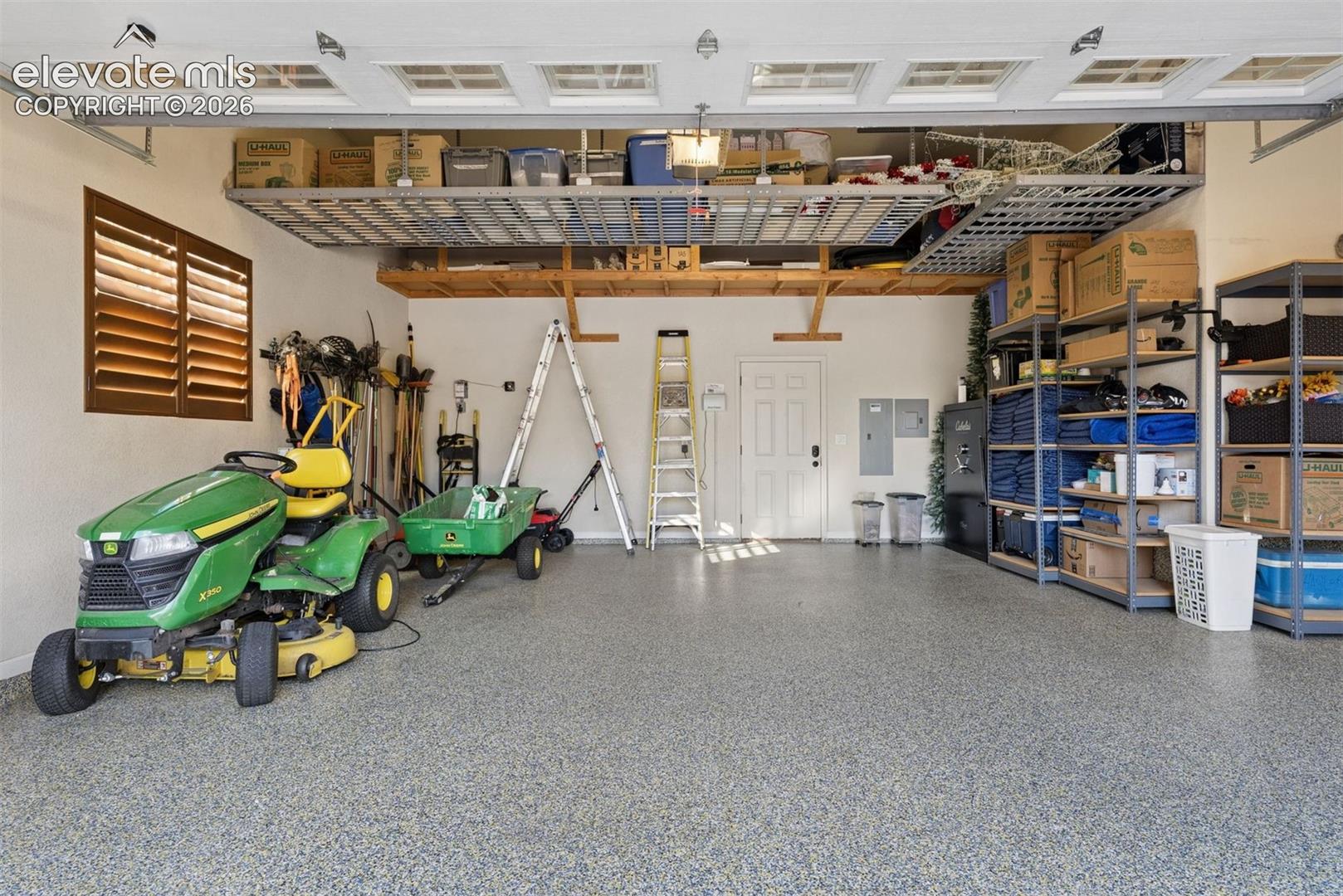 Multi-car garage featuring epoxy-coated flooring, overhead metal storage racks, wood-shuttered window, and insulated pedestrian entry door