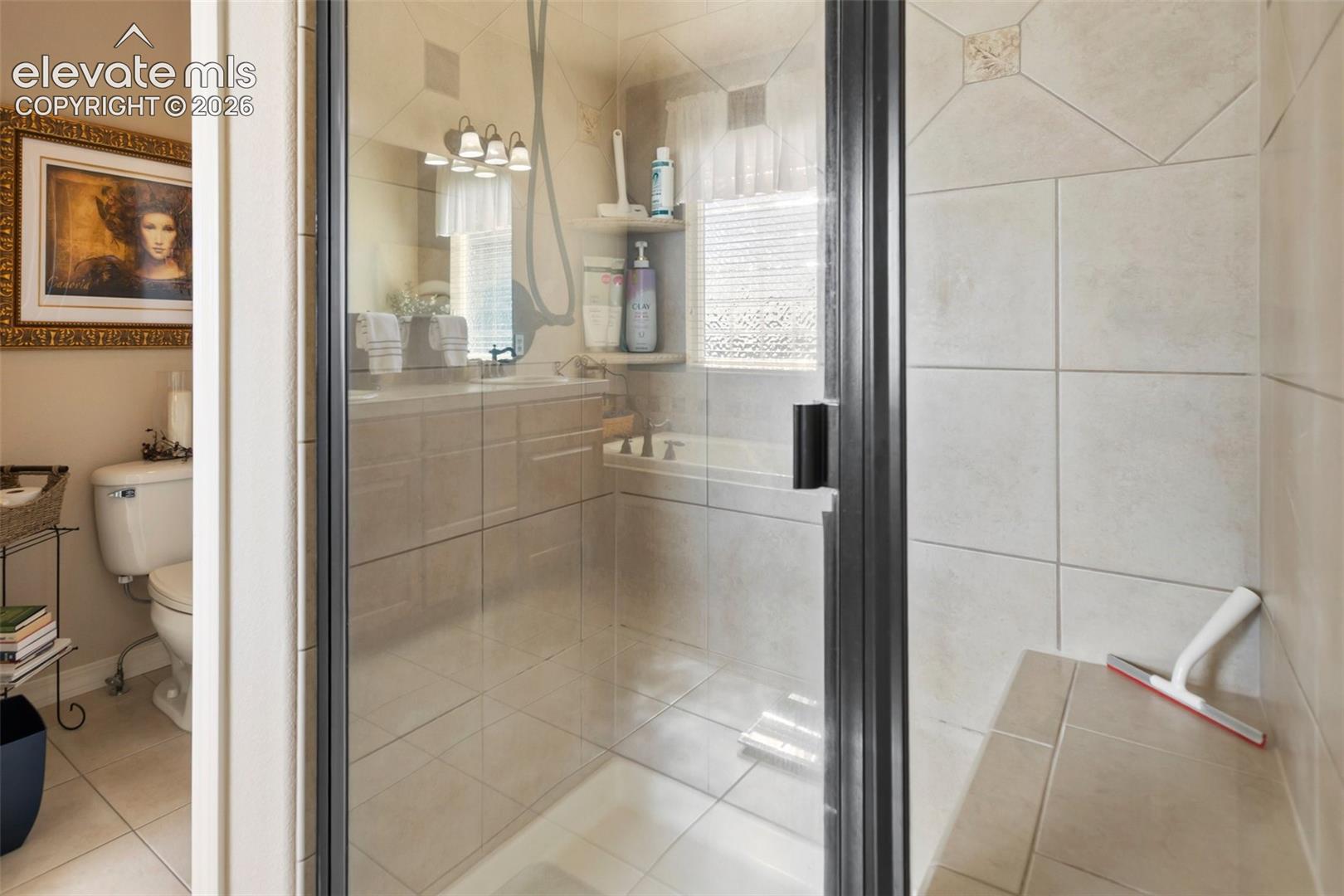 Enclosed shower featuring a tiled built-in bench and glass door, neutral wall tile, integrated soaking tub, vanity cabinetry, and three-bulb vanity lighting
