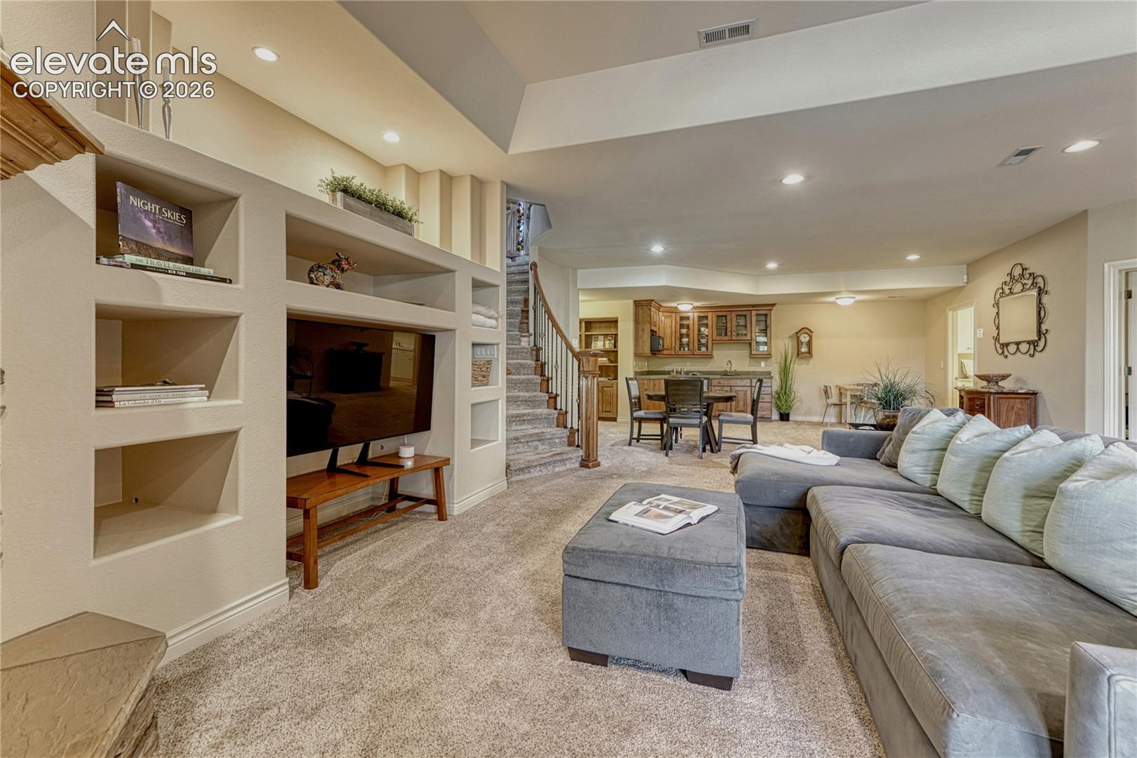 Open floor plan featuring recessed lighting, a built-in media shelving unit, a tray ceiling, and a staircase with wood-capped railing