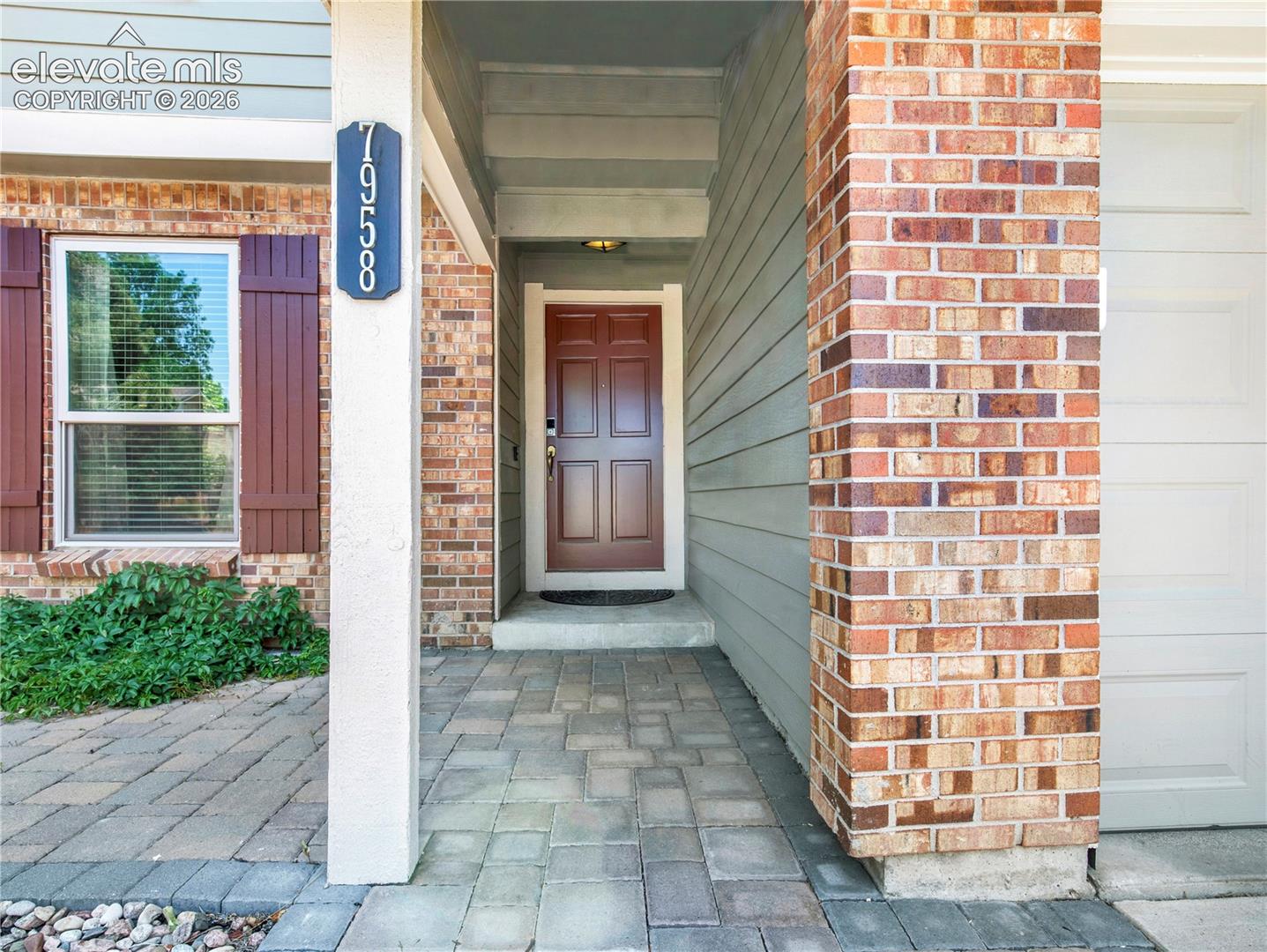 Covered entryway featuring a six-panel wood-finish door, multi-tonal brick facade, horizontal lap siding, and stone-paver walkway