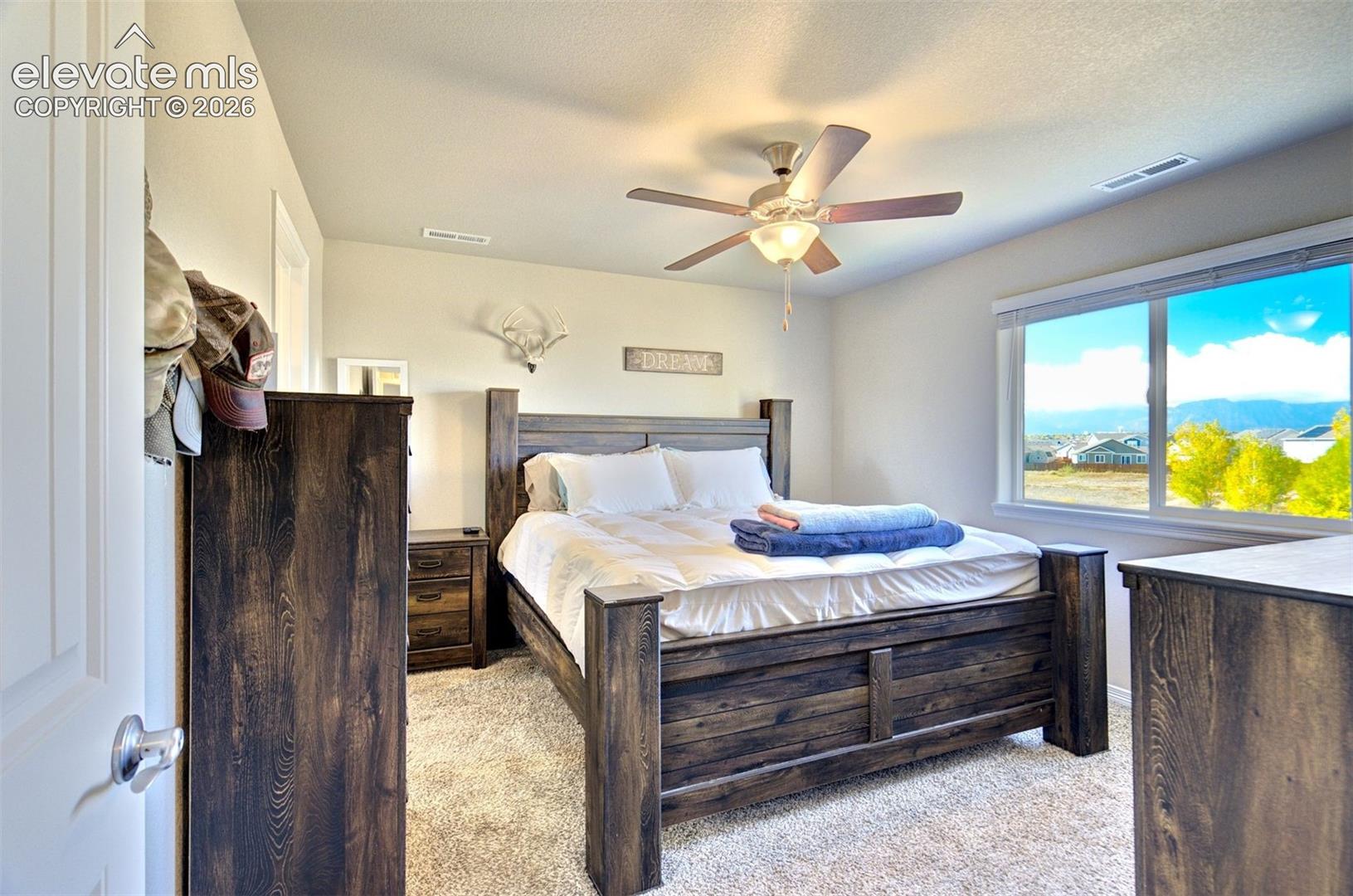 Neutral wall tones, carpeted flooring, large window with mountain scenery, and ceiling-mounted light fixture with fan