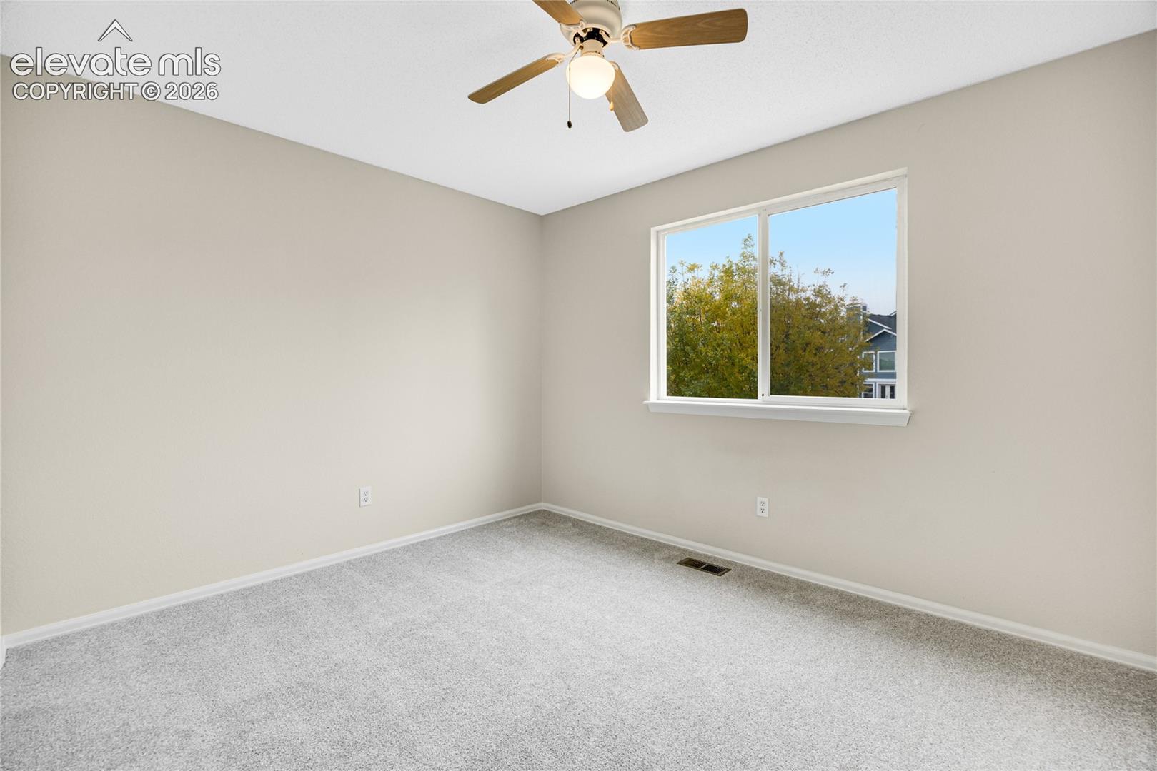 Neutral-toned interior space featuring wall-to-wall carpeting, a multi-pane sliding window, and a central ceiling fan with an integrated light fixture
