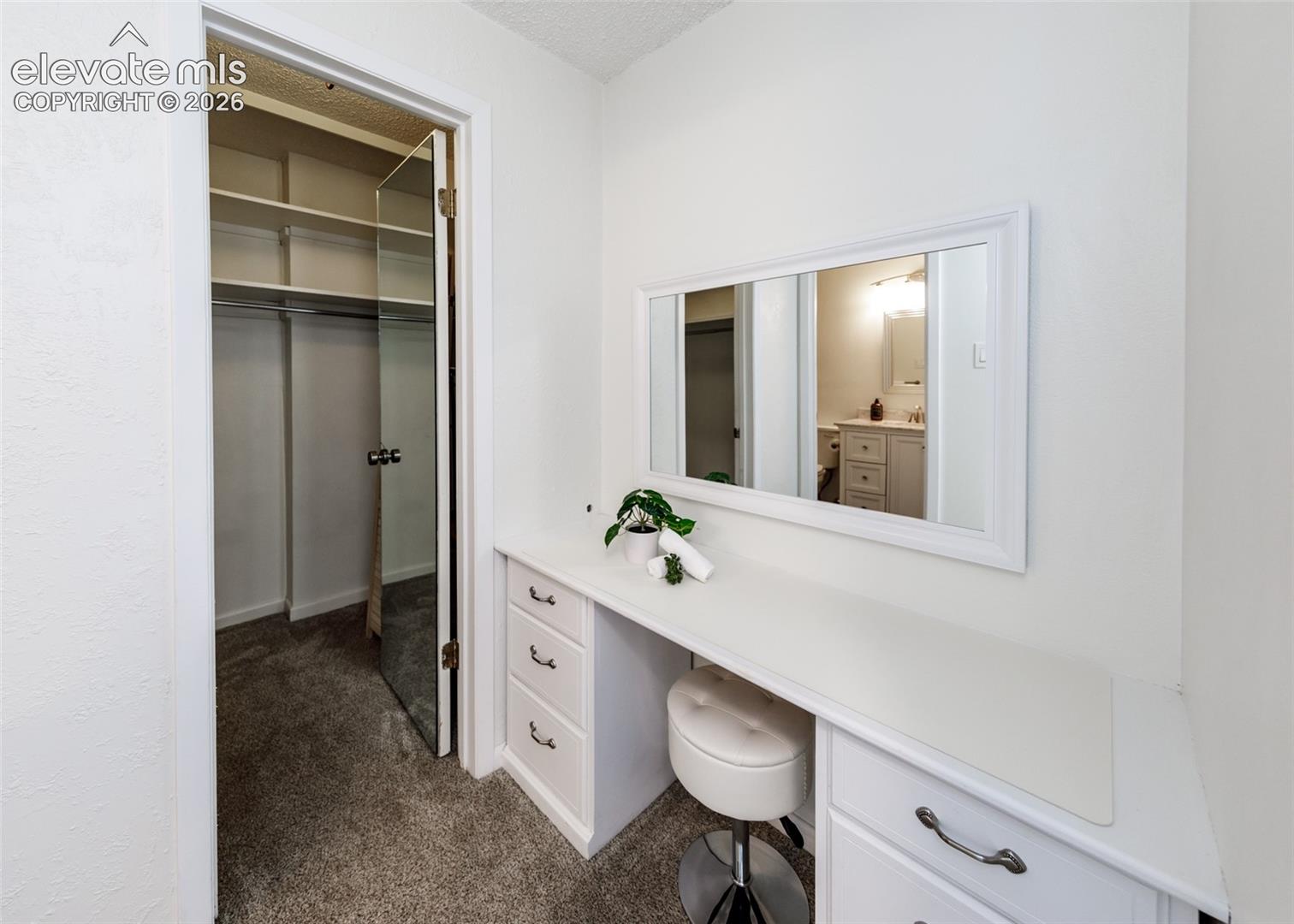Built-in white vanity with storage drawers, framed wall mirror, and walk-in closet with integrated shelving