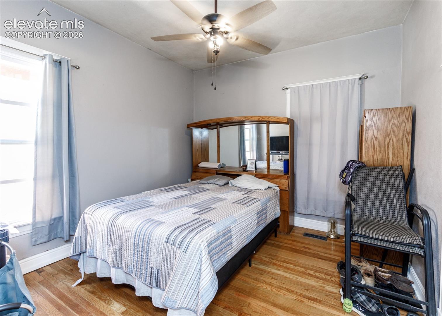 Hardwood flooring, painted walls, ceiling fan with integrated lighting, and two windows with curtain rods