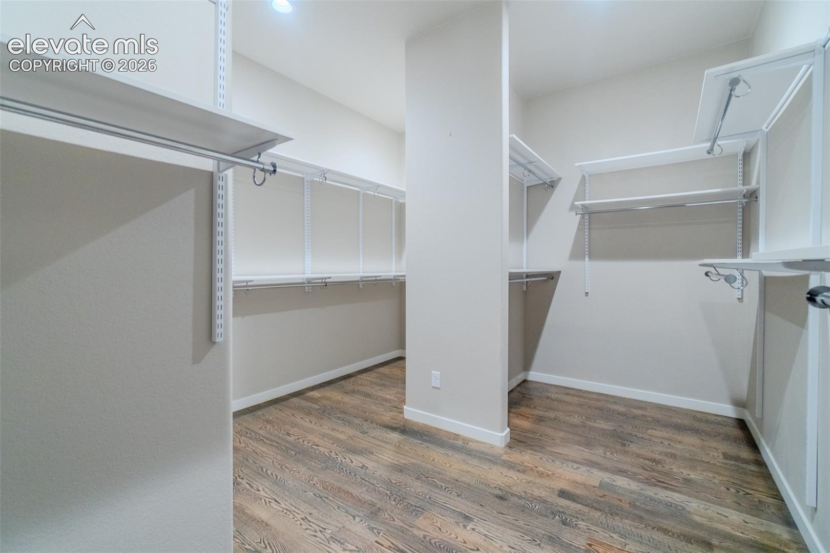 Spacious walk-in closet featuring wood-finish flooring, white adjustable shelving, and multiple hanging rods