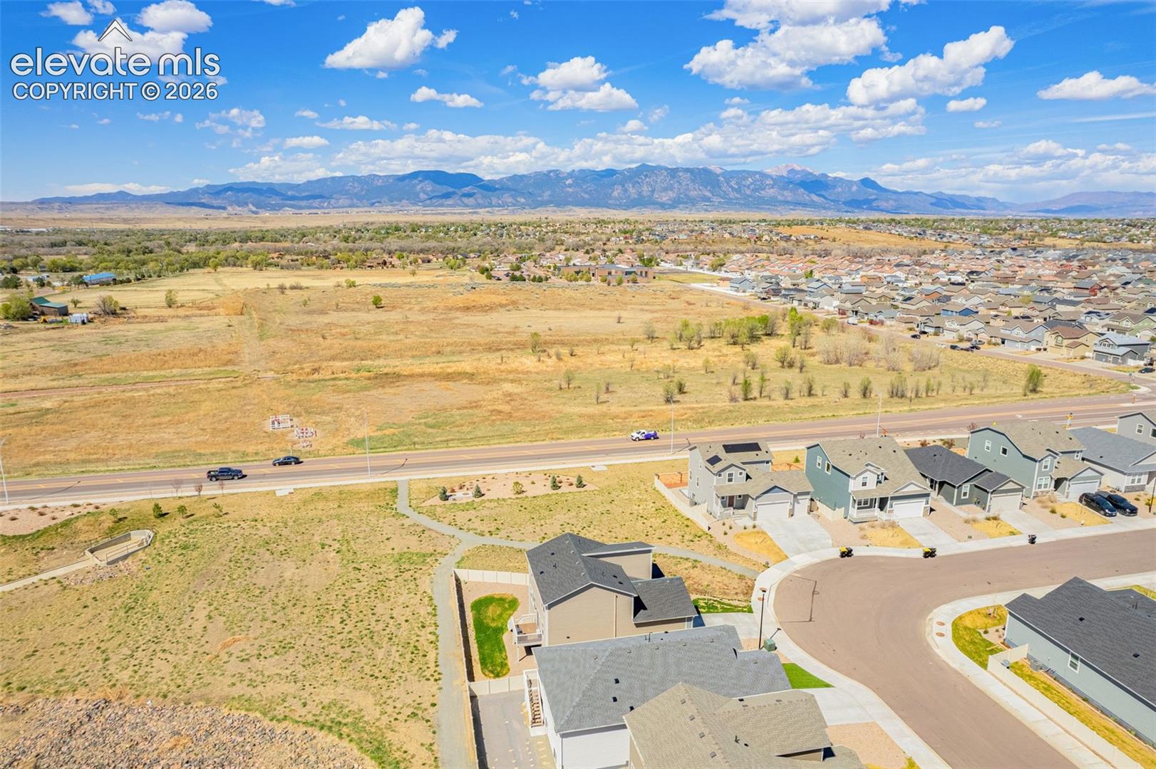 Expansive mountain range backdrop, residential neighborhood setting, curved street layout, paved roadways, and varied home exteriors