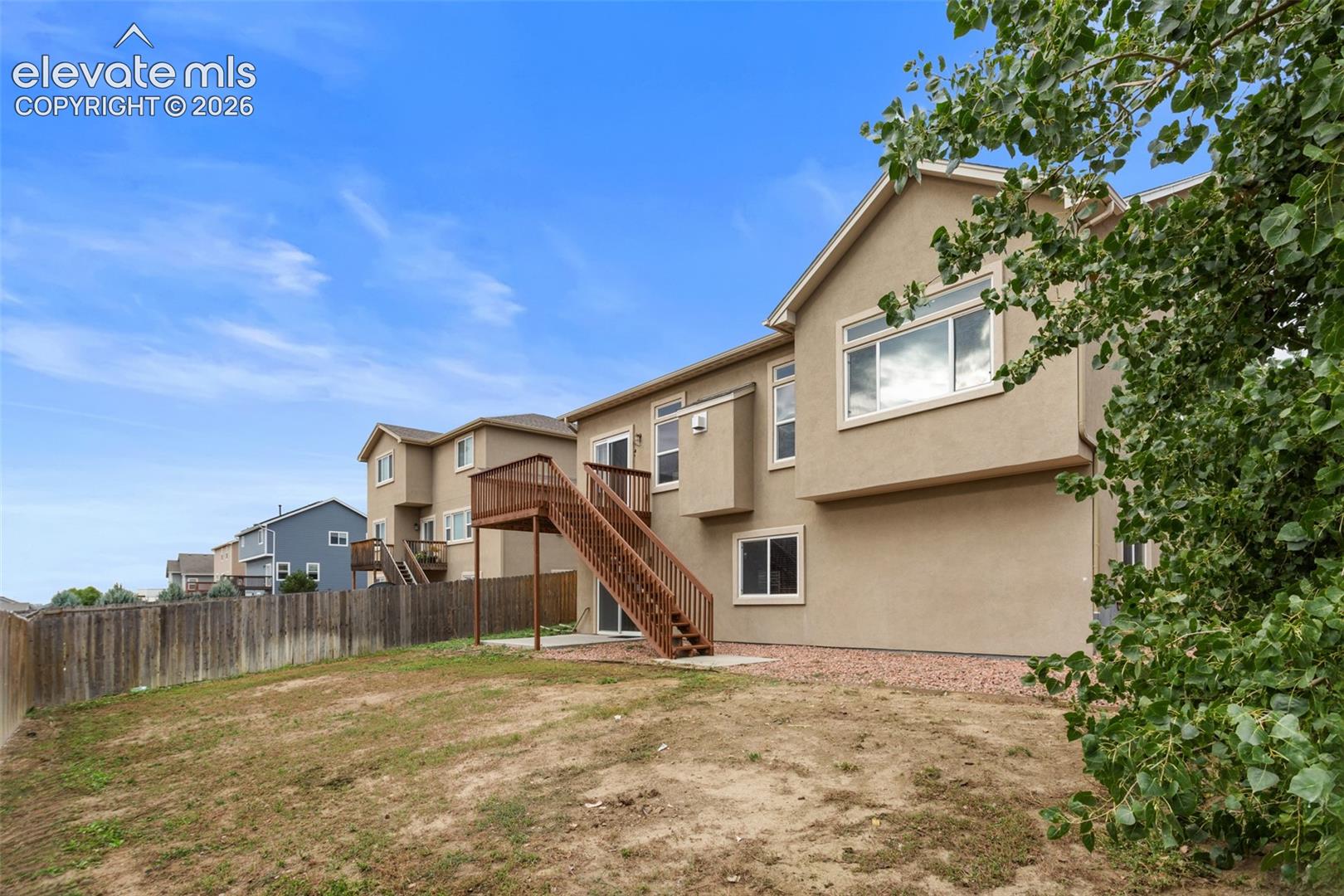 Rear exterior featuring a beige stucco facade, raised wooden deck with stairs, sliding glass doors, and a partial wood fence
