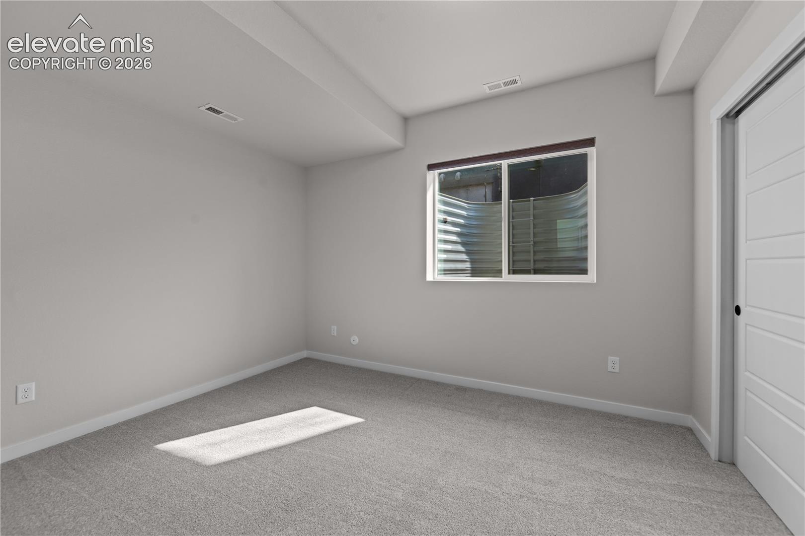Neutral interior space featuring neutral wall paint, wall-to-wall carpeting, a sliding window with an egress well, and a horizontal panel door