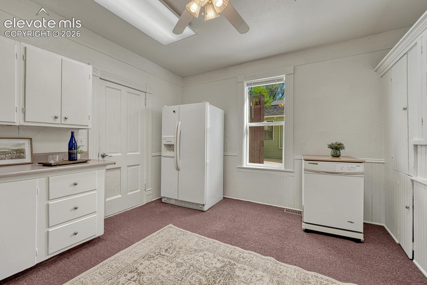 White cabinetry, integrated appliances, single window, beadboard wall paneling, and a ceiling fan