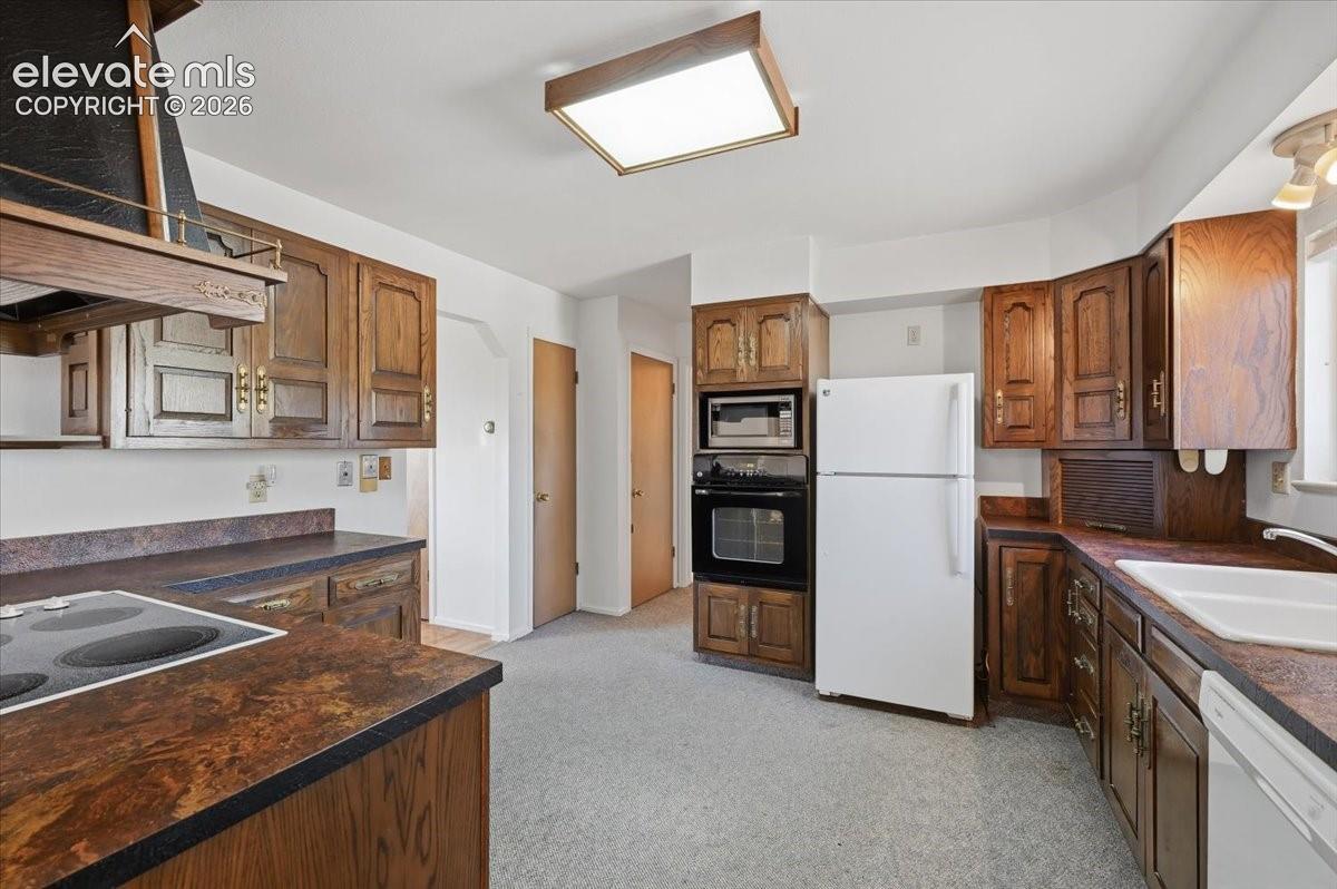 Kitchen featuring stained wood cabinetry, built-in double ovens, a drop-in electric cooktop, laminate countertops, and a dual-basin sink