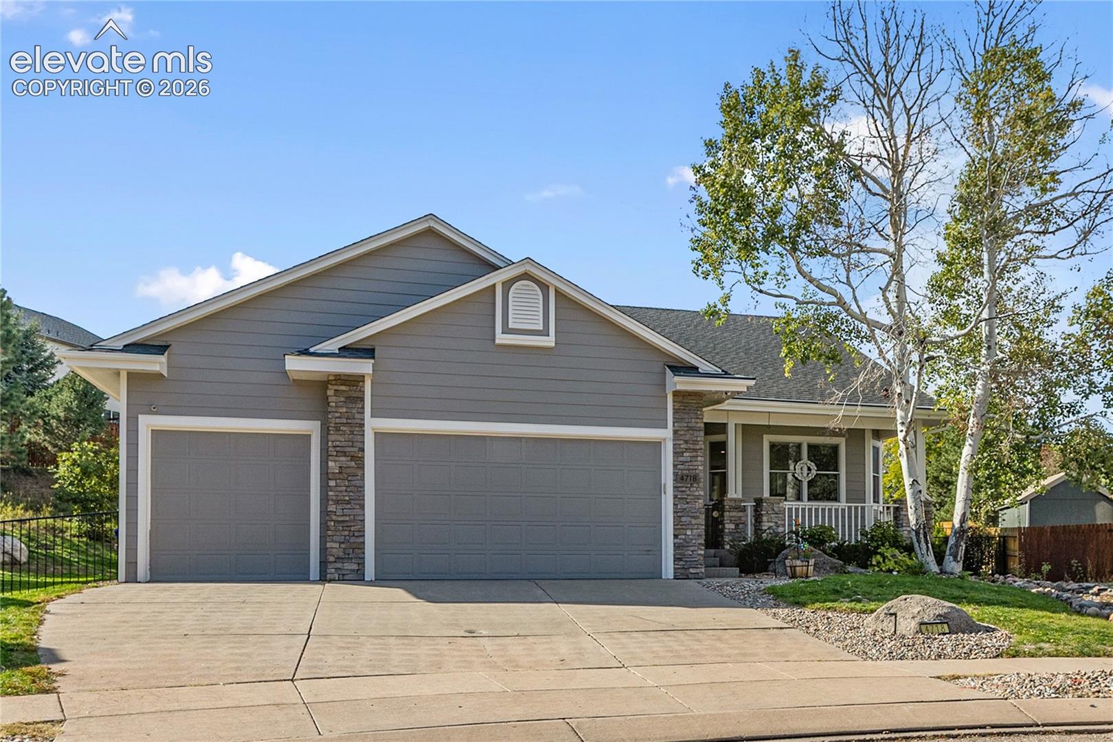 Gray siding exterior with stone accents, featuring a two-car garage, covered entry porch, and mature landscaping