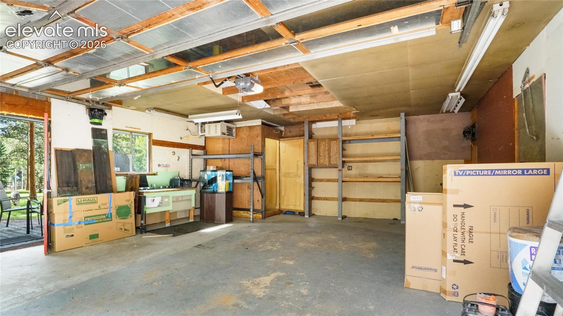Garage featuring a built-in workbench, exposed beam ceiling, fluorescent lighting, and a window