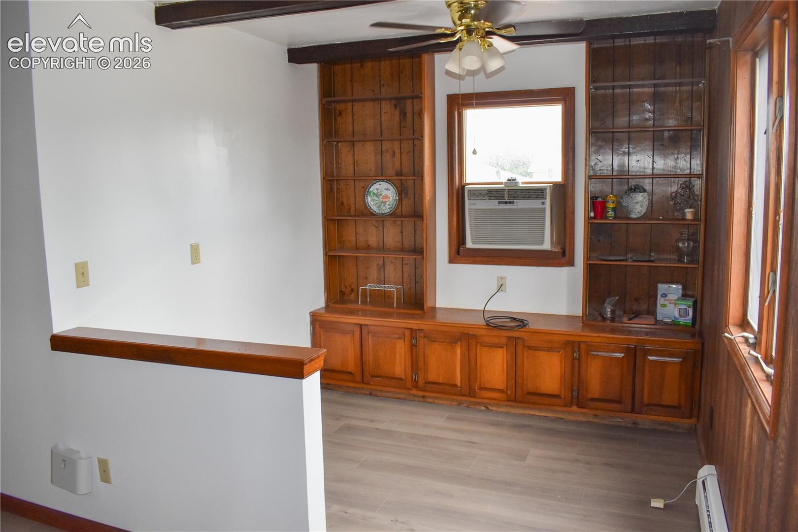 Built-in wood cabinetry with shelving, wood-finish flooring, exposed ceiling beams, and a ceiling fan