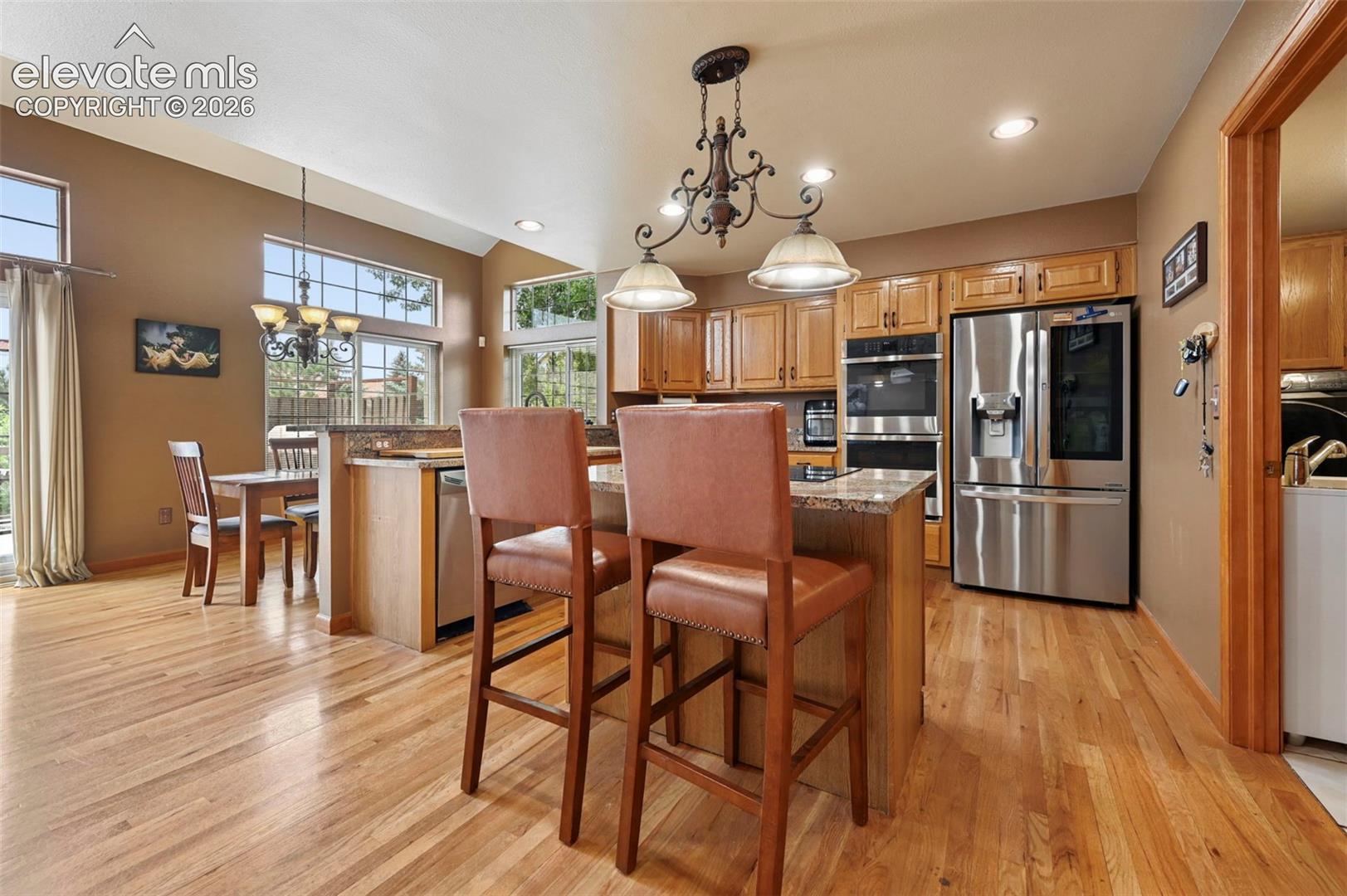 Kitchen featuring wood-finish flooring, a central island with countertop seating, stainless steel double ovens, and a stainless steel refrigerator