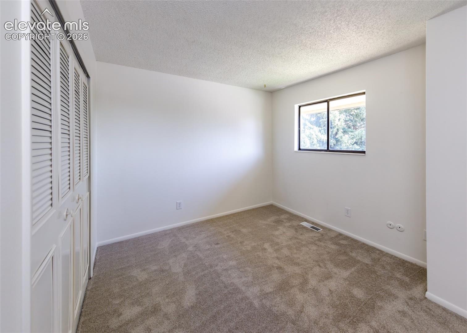Neutral-toned carpeting, white walls, and closet storage featuring louvered bi-fold doors