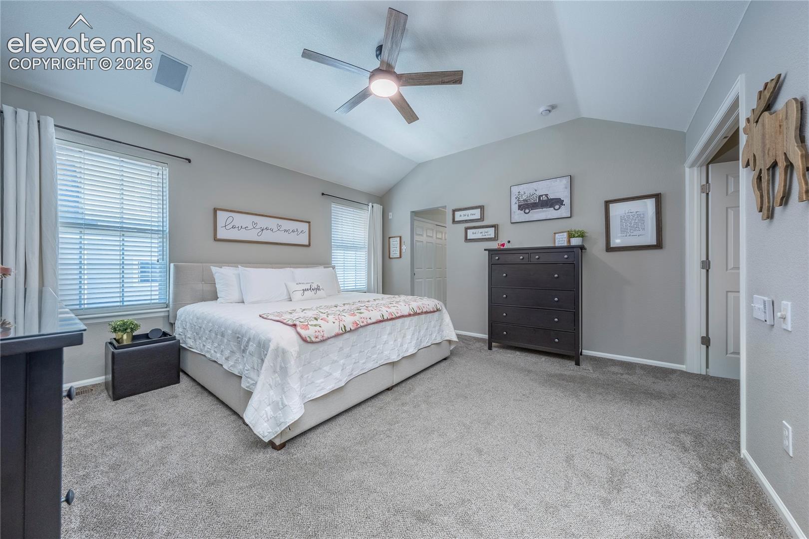 Vaulted ceiling, ceiling fan with integrated lighting, neutral wall palette, carpeting, and multiple windows