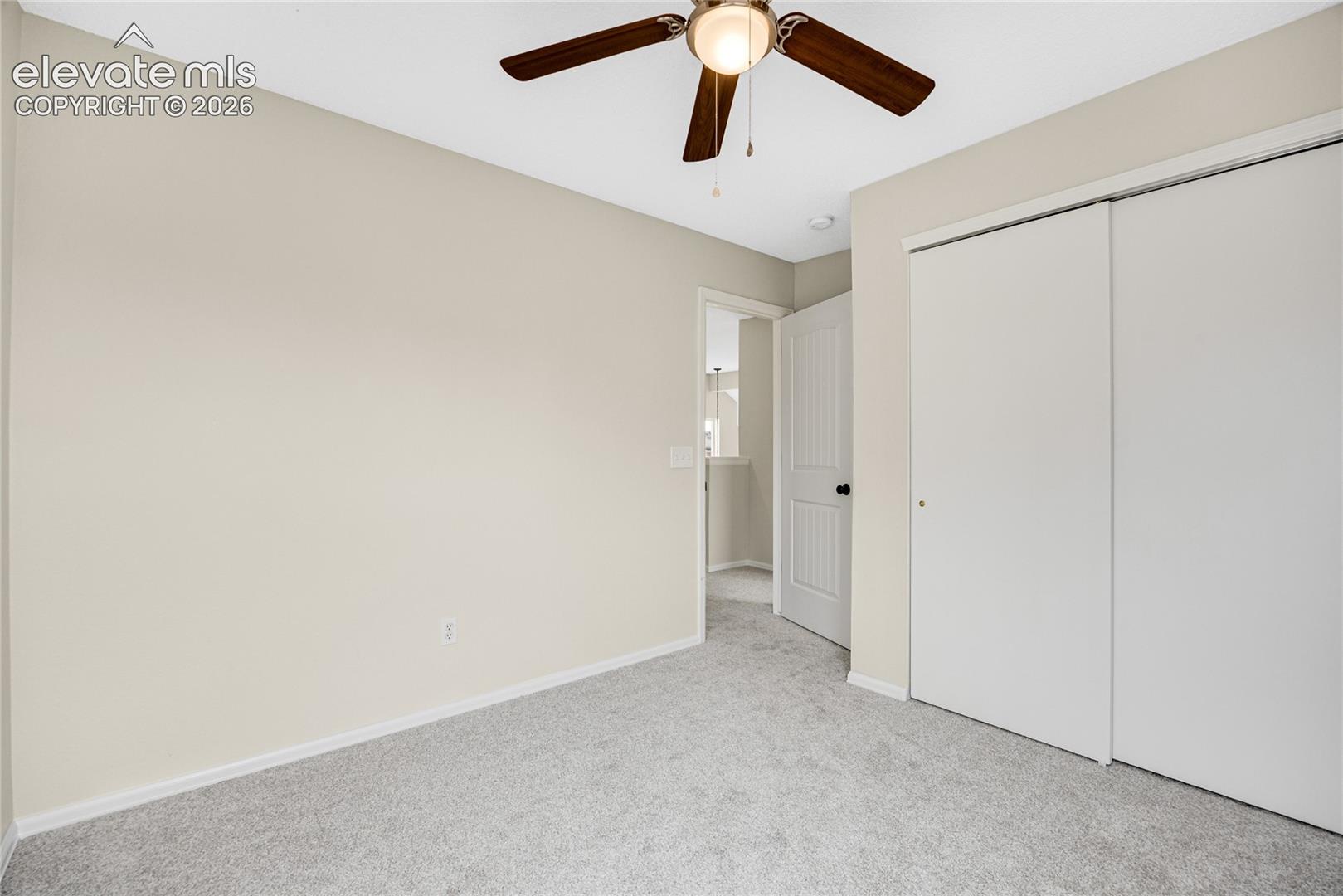 Room featuring neutral wall paint, wall-to-wall carpeting, a ceiling fan with integrated lighting, and a dual-panel sliding closet door
