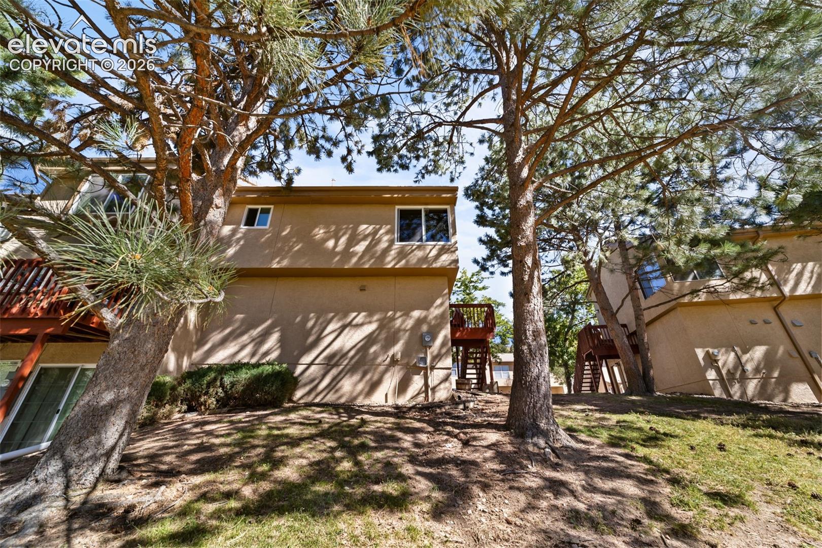 Exterior elevation featuring textured siding, multi-level wood-finished decking, and mature pine trees on a sloped lot