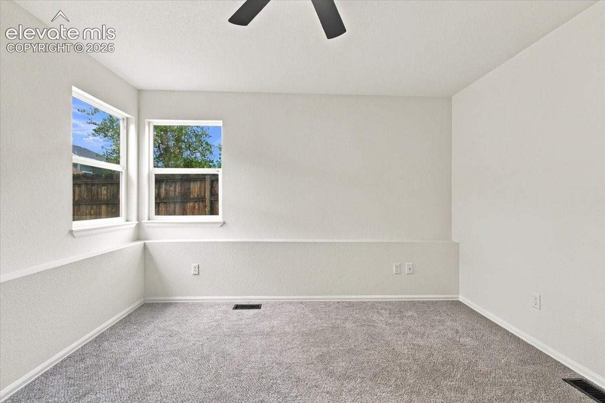 Neutral-toned interior space featuring light-colored wall texture, wall-to-wall carpeting, dual windows, and a ceiling fan with matte black finish