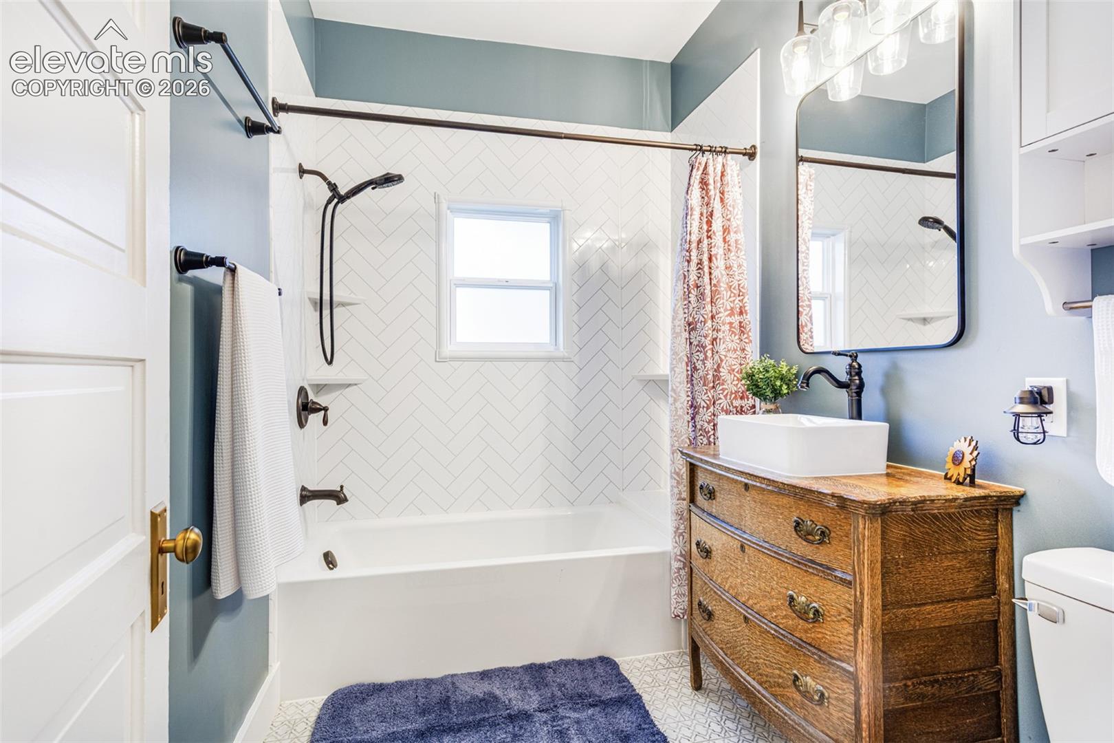Bathroom featuring a white bathtub, herringbone pattern tile surround, black-finish shower fixtures, and a window