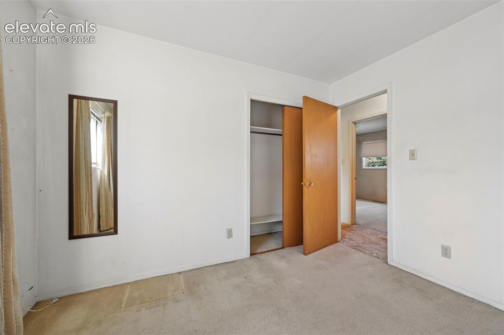 Bedroom 3 with neutral-toned carpeting, a built-in closet with natural wood-finish doors, and an inset wall mirror